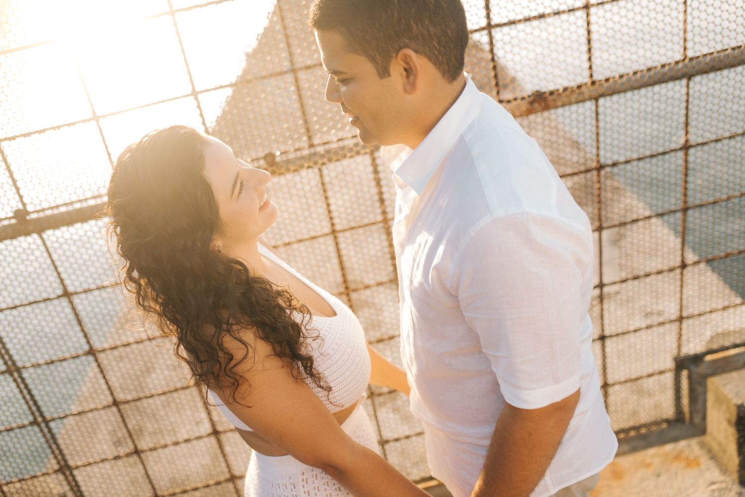 Romantic couple in white clothing embracing during golden hour photoshoot.