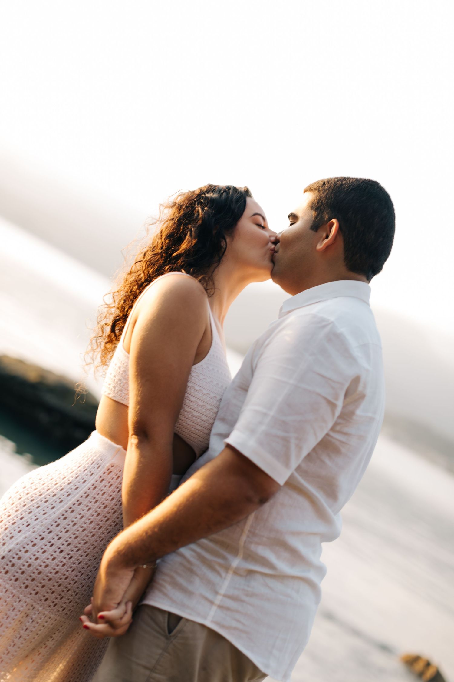 Intimate moment between a couple sharing a sunset kiss by the water.