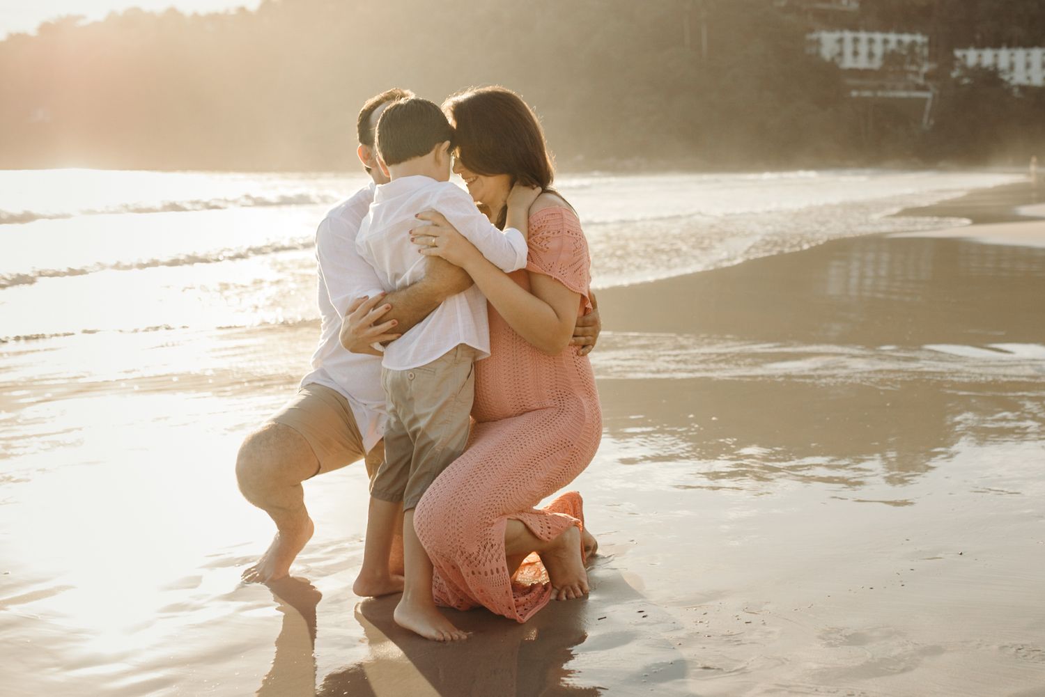 Couple embracing romantically in shallow ocean water as sun sets behind them.