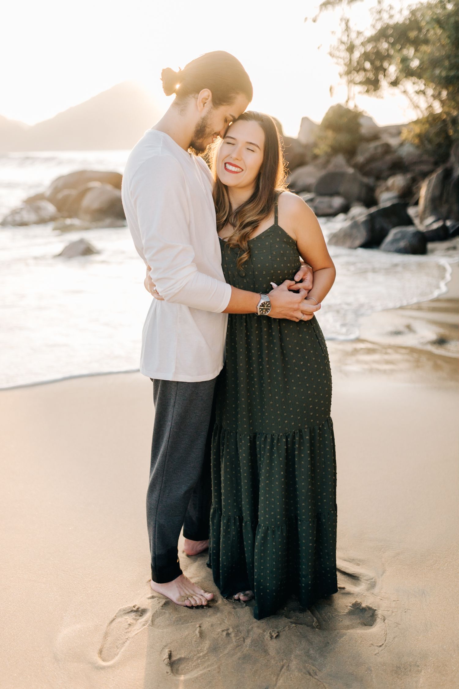 Joyful couple sharing intimate moment during sunset beach photography session near rocky shore.