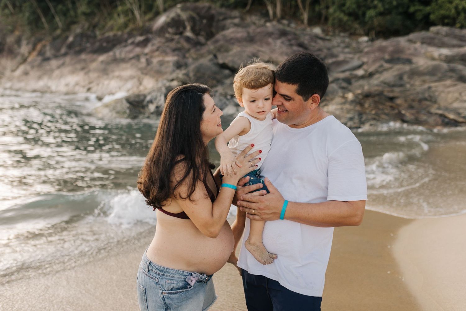 Candid family beach photoshoot showing joyful interactions near coastal rocks.