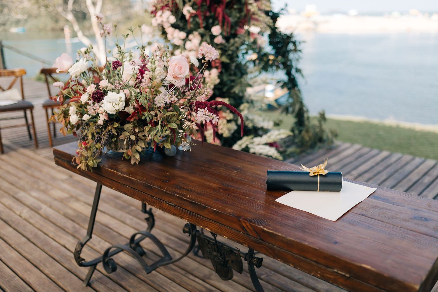 Rustic wooden tables decorated with floral arrangements on a lakeside deck.