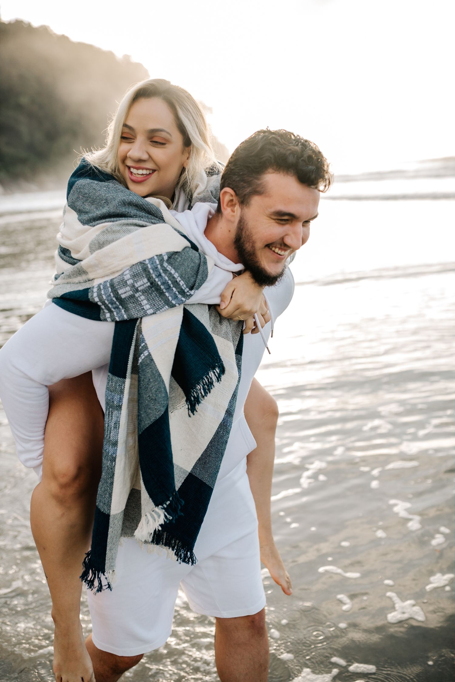 Candid moment of couple sharing laughter during piggyback ride on beach.