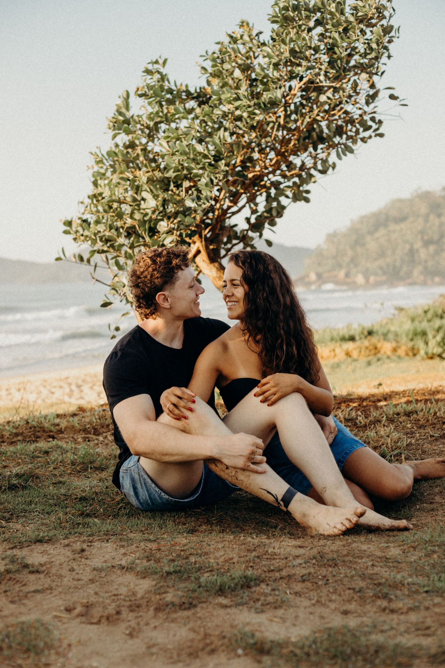 Couple relaxing under tree on coastal hillside during golden hour.