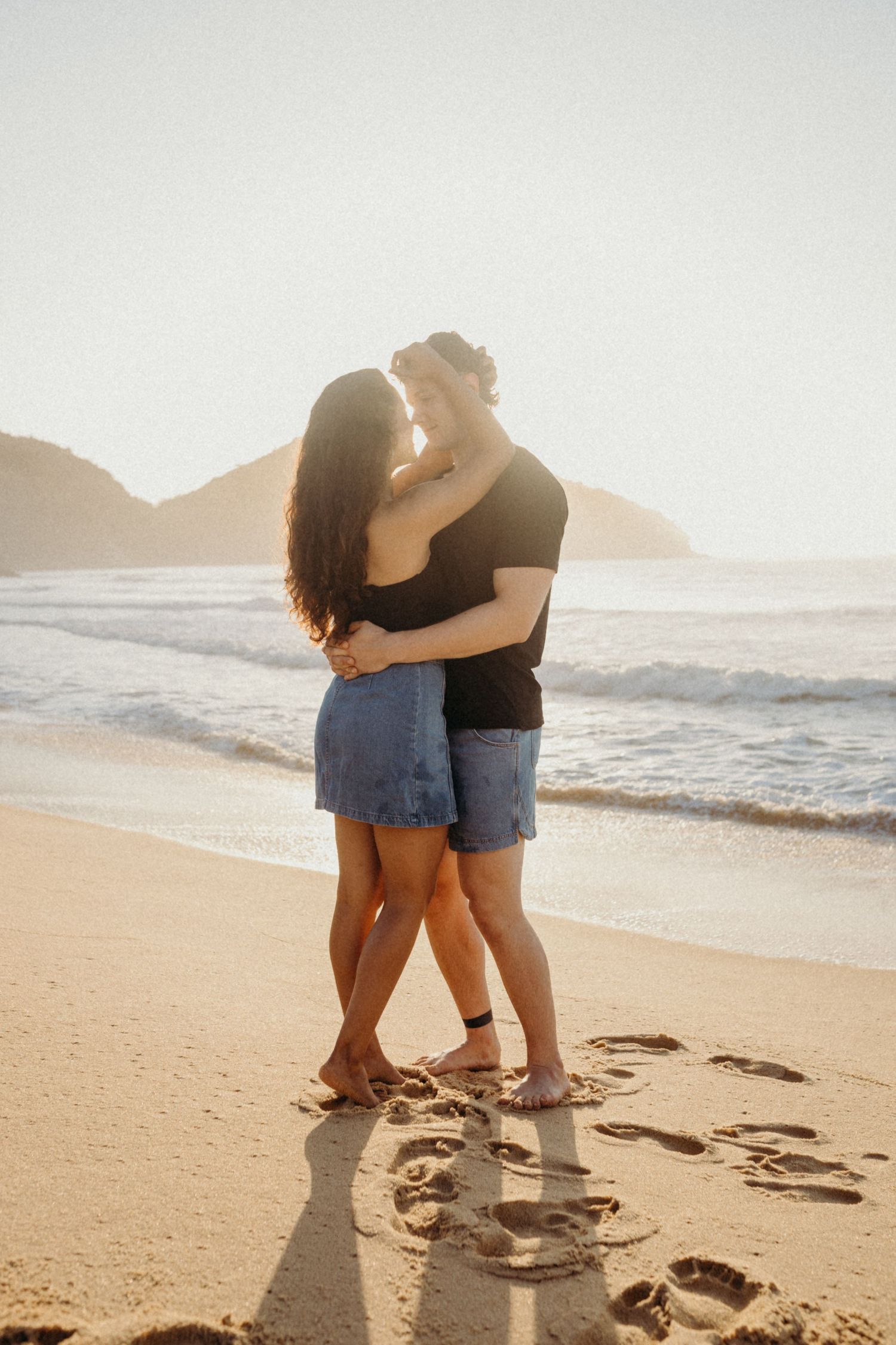 Romantic beachside moment between couple embracing on sandy shore during golden hour.