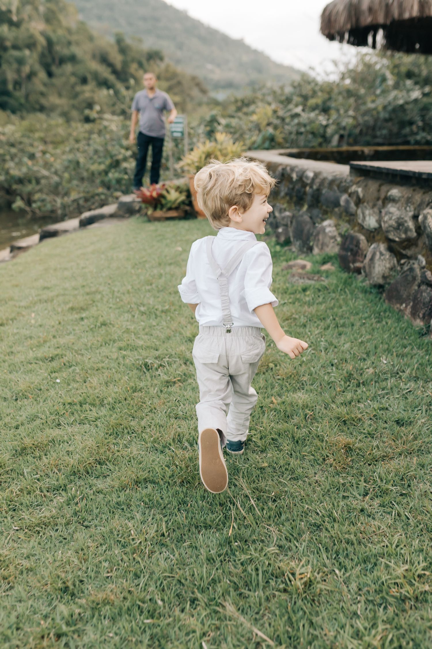 A small child in white clothing runs playfully across a grassy hillside area.