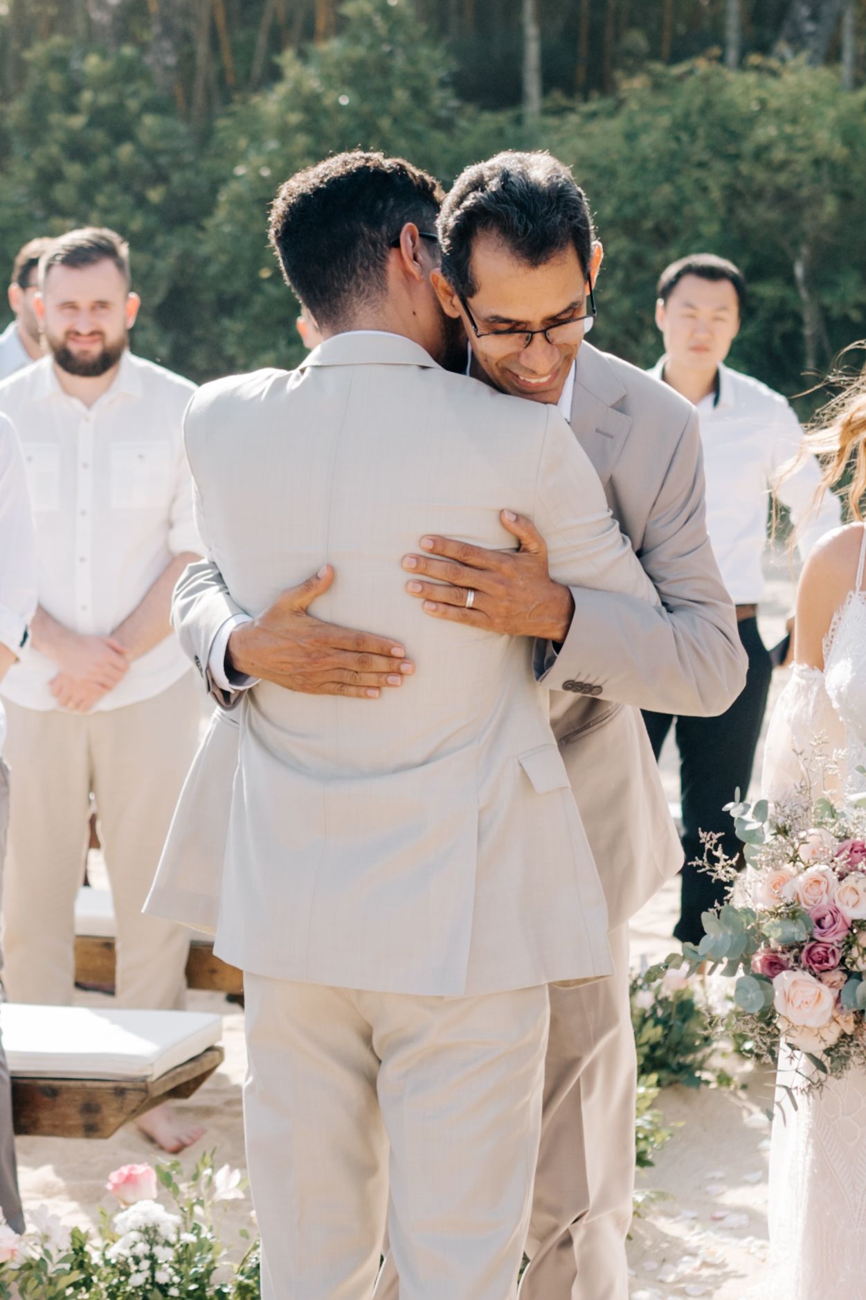 Two people embrace during an outdoor wedding ceremony while guests look on.