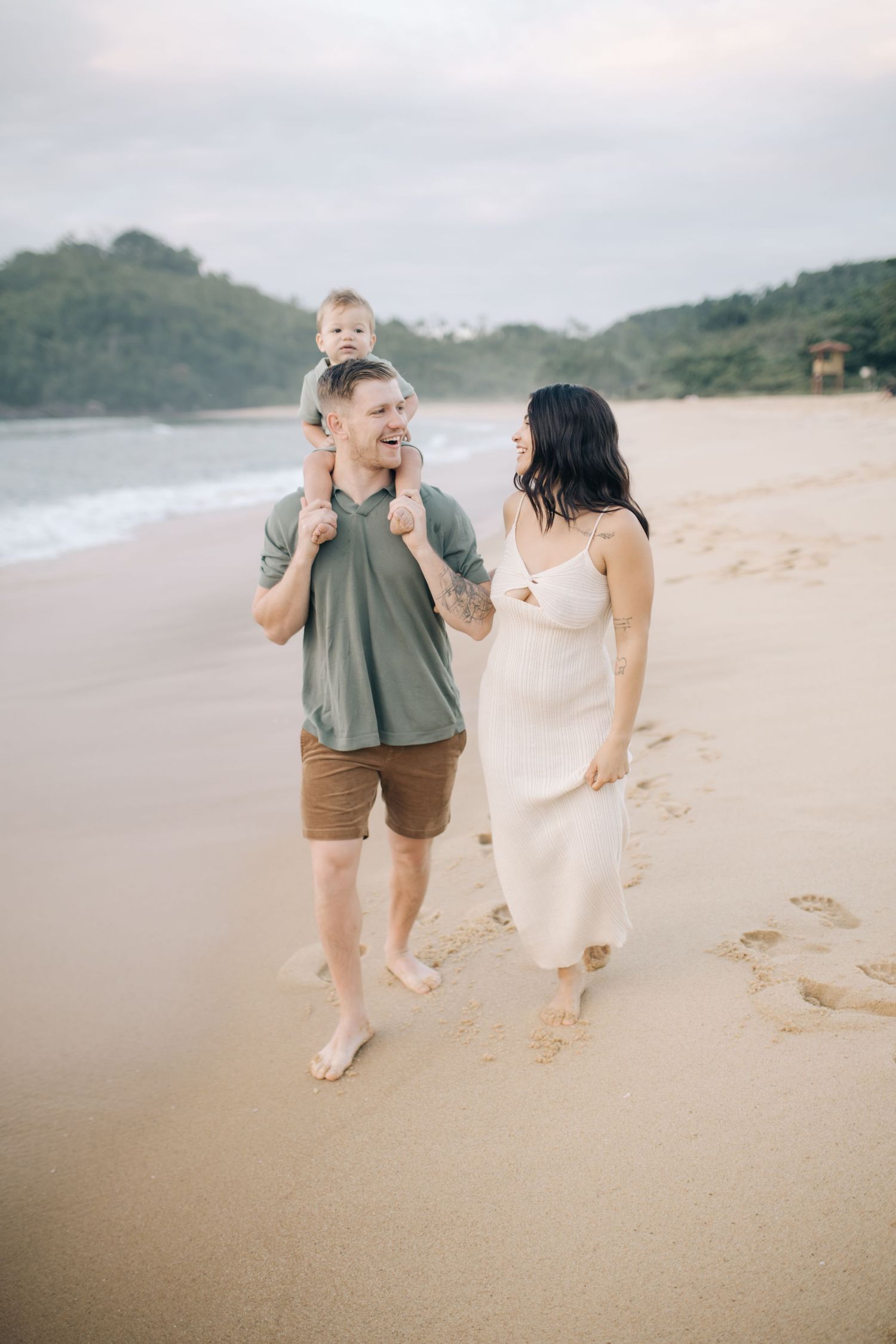 A family walks along a sandy beach leaving footprints by the ocean.