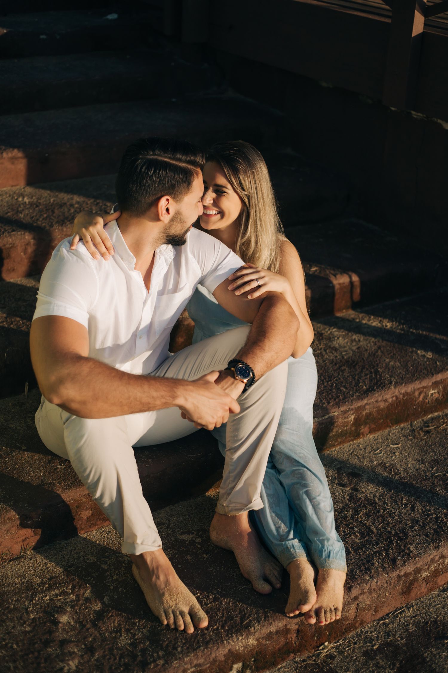 Intimate couple moment captured on rustic steps during golden hour lighting.