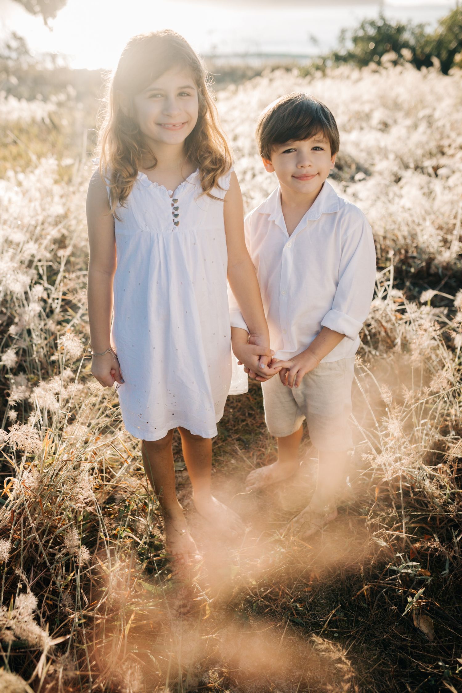 Children stand together in a field of wild grass during sunset.
