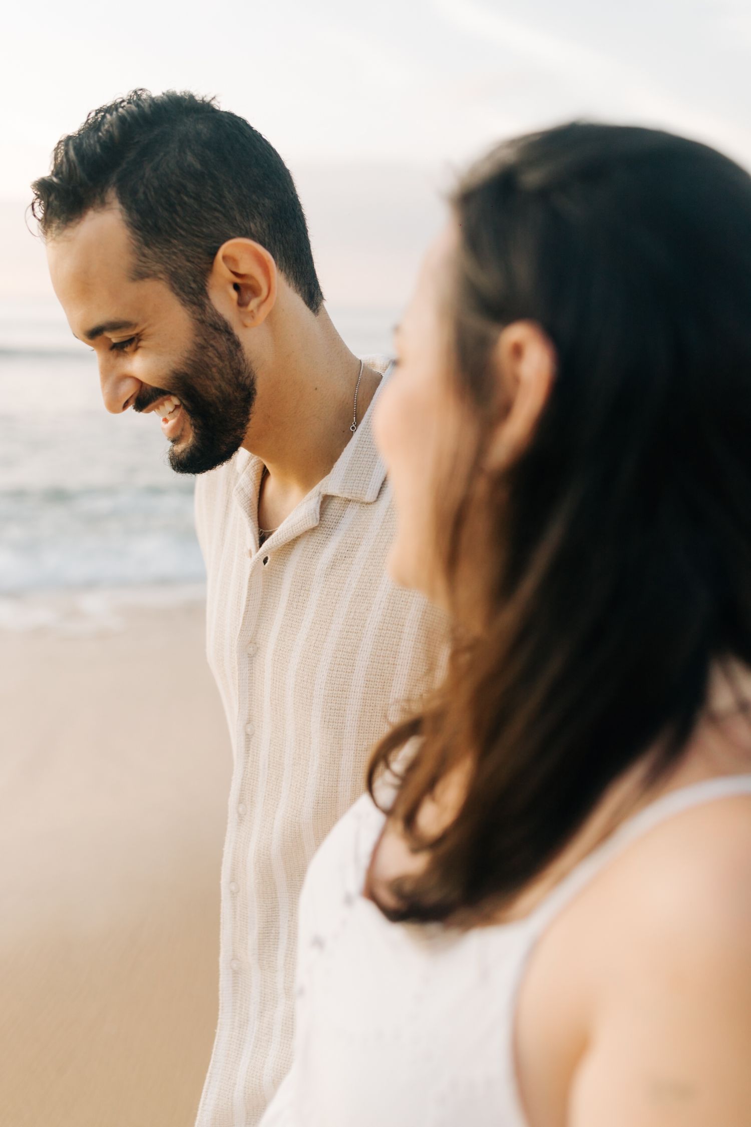 Couple shares intimate moment on beach with mountains in background at sunset.