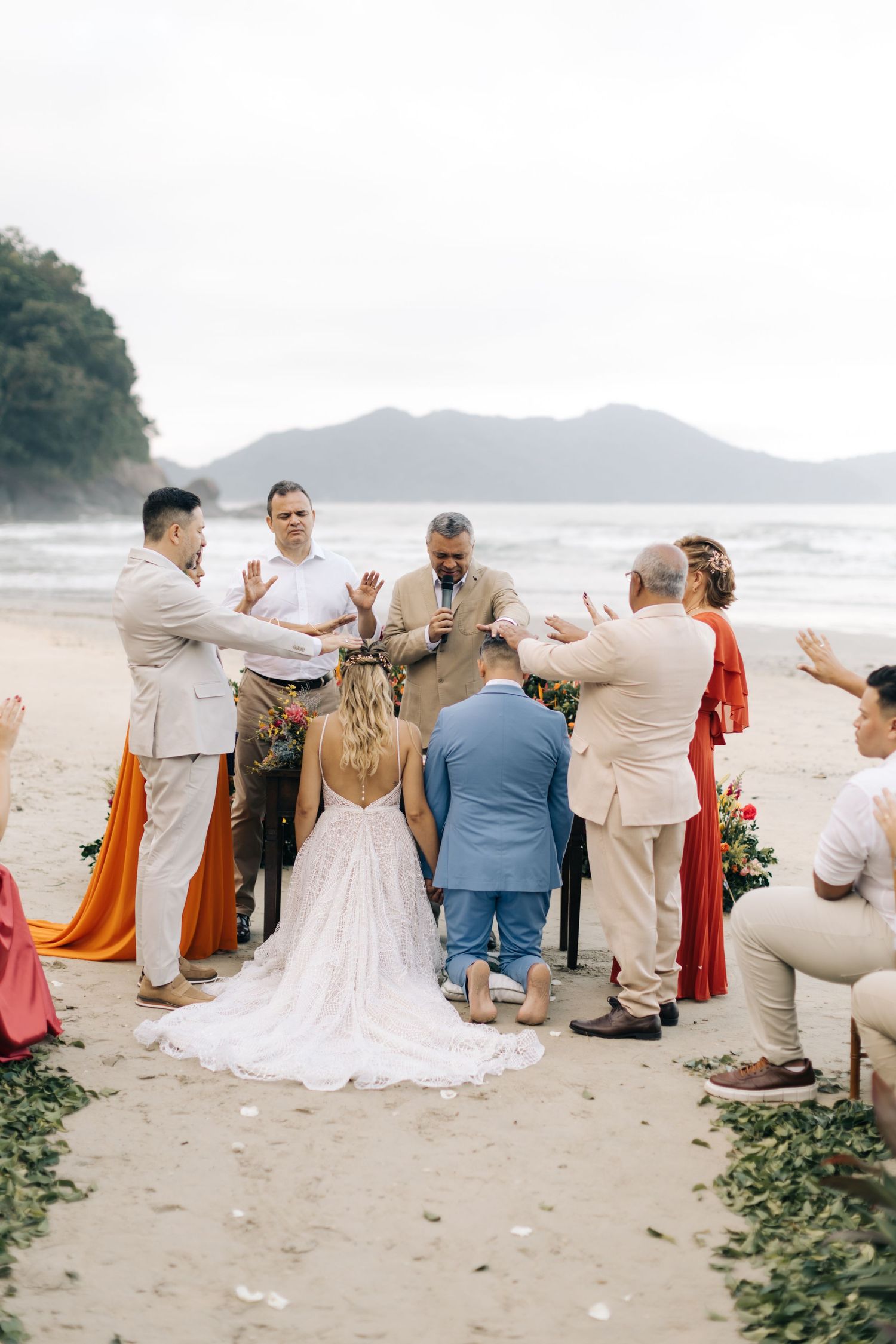 Beach wedding ceremony with guests in tan and coral attire against a coastal landscape.