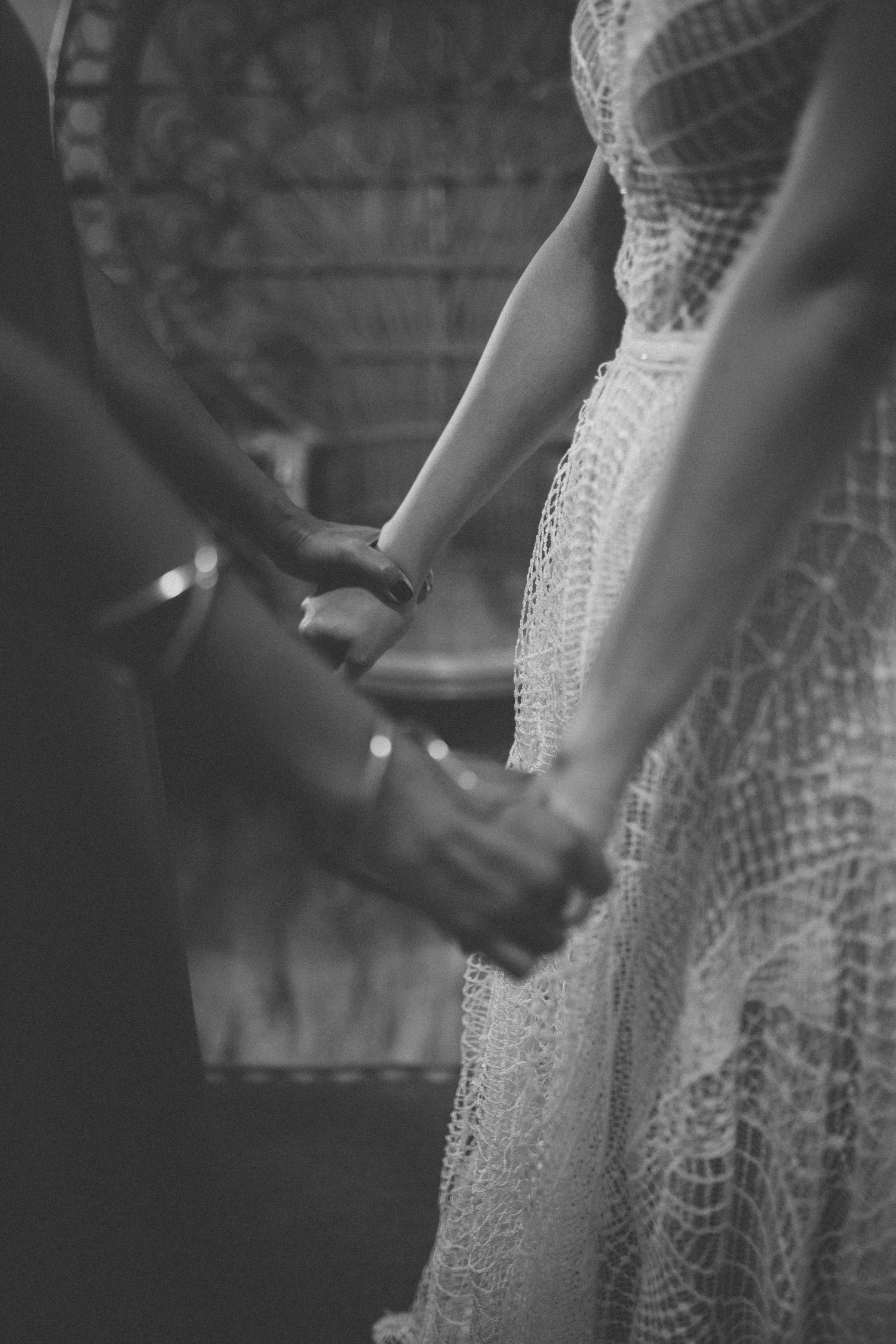 Close-up of hands holding during wedding ceremony, bride wearing detailed lace dress.