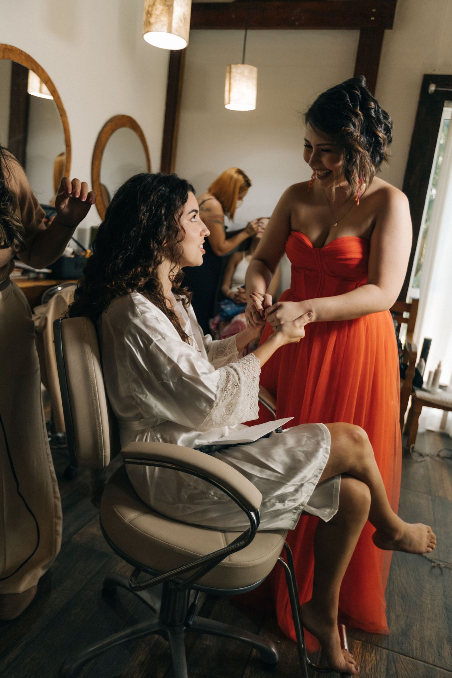 Two people in formal attire sit in a getting-ready room with mirrors and lighting.