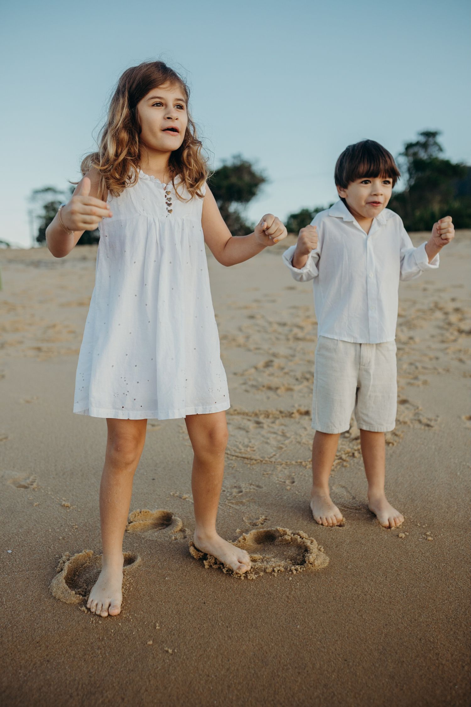 Children's bare feet around a heart drawn in wet sand on a tropical beach.