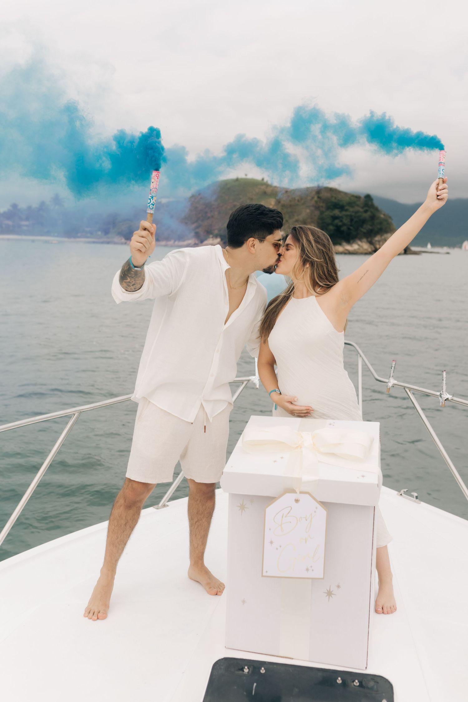 Couple embracing on boat deck with blue smoke flares and coastal scenery.