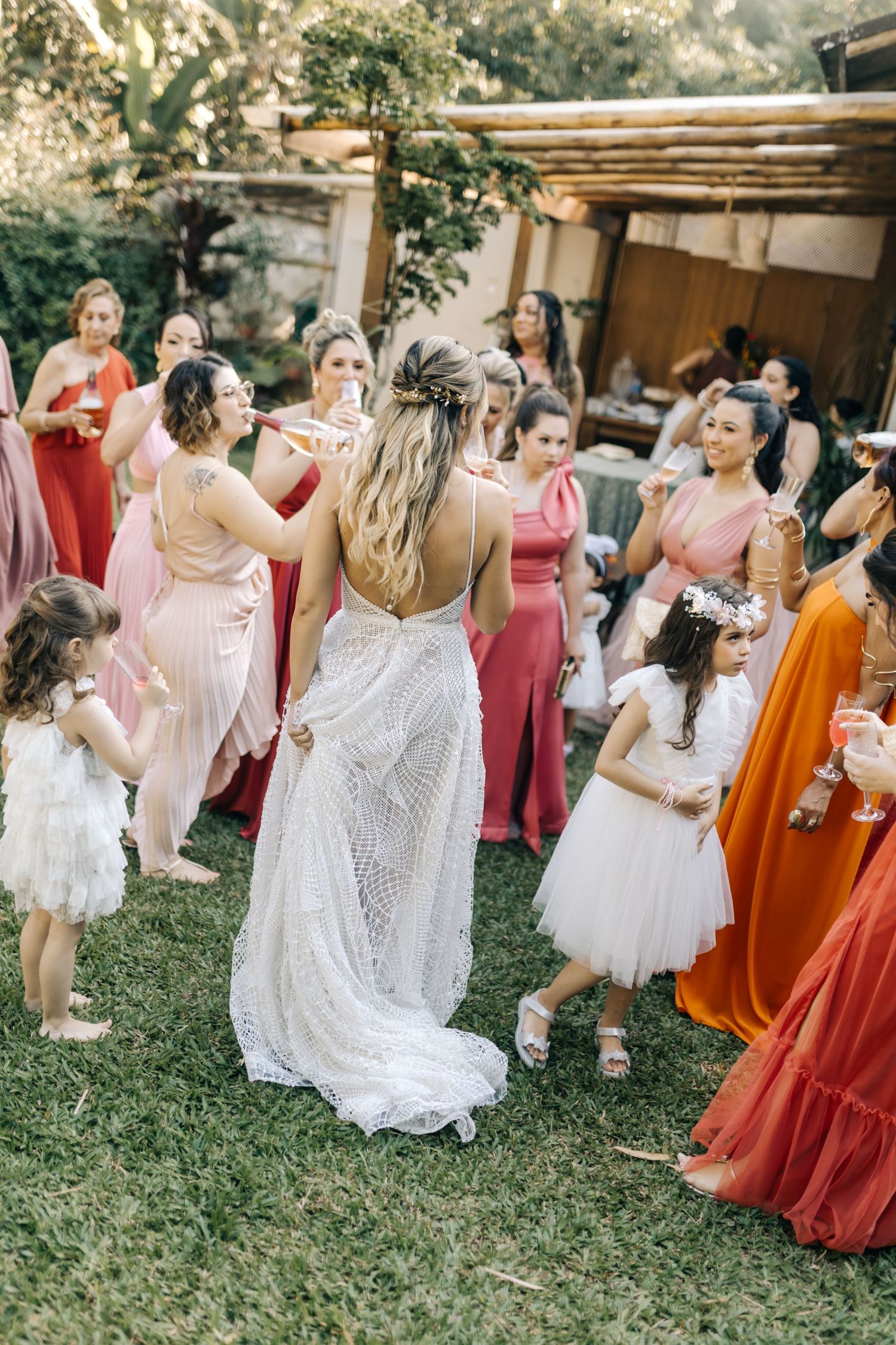 Wedding celebration on a lawn with attendees in colorful dresses dancing under a wooden pergola.