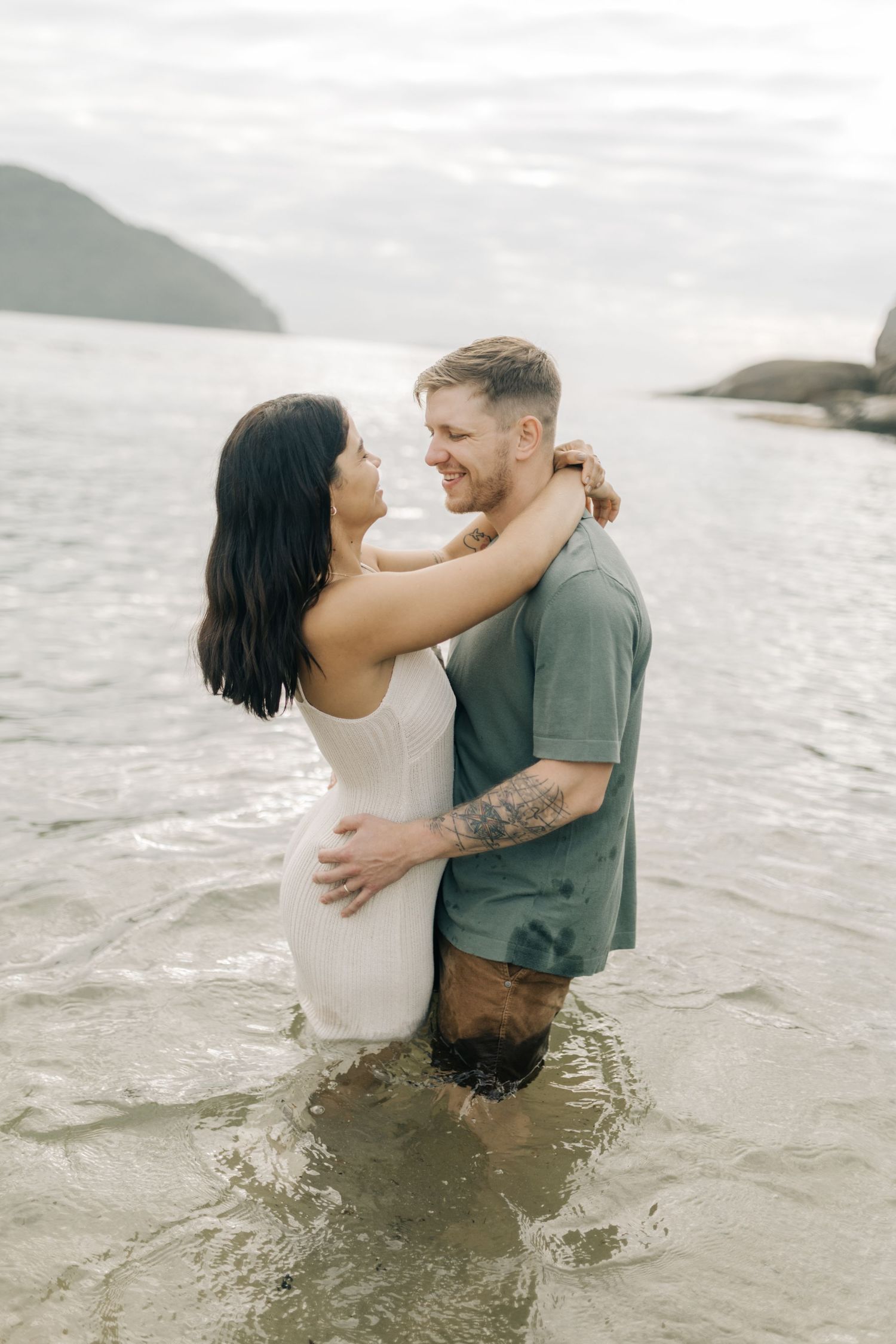 Couple sharing tender moments while standing in ocean waves at beach.