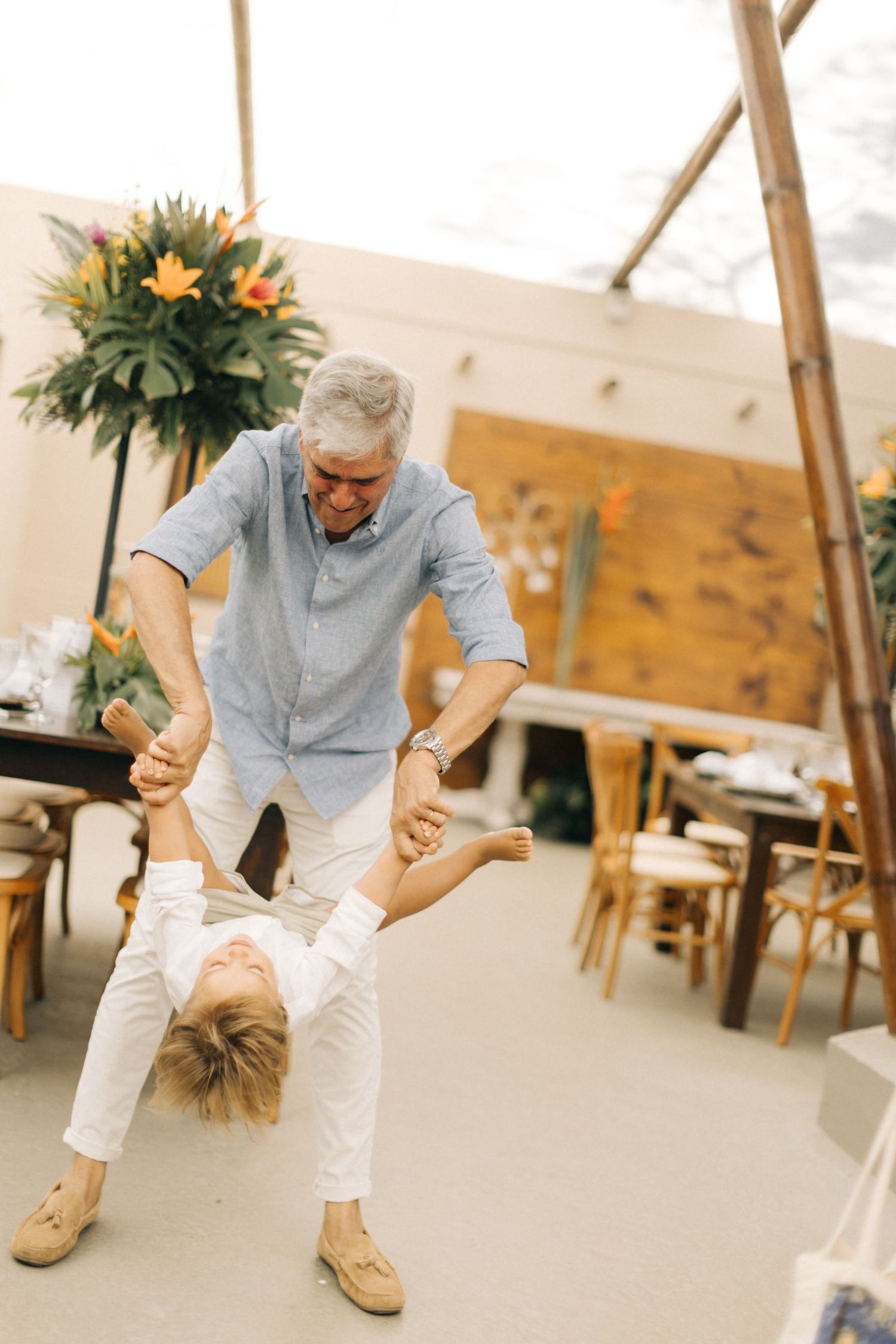 A person in light clothing bends down playfully in a room with floral decorations.