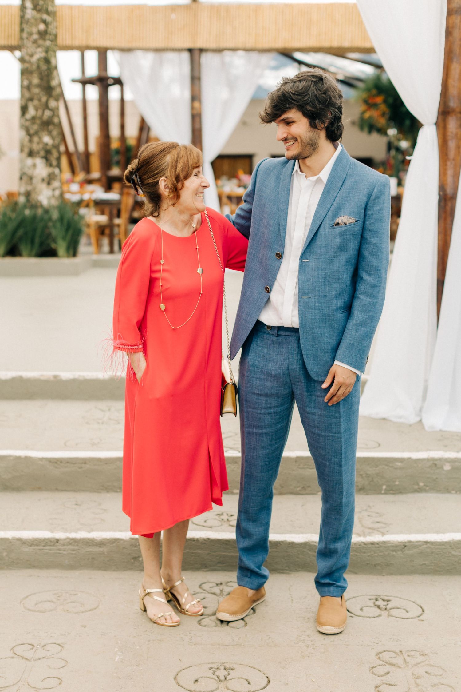 Couple in red dress and blue suit standing together on decorated outdoor patio.