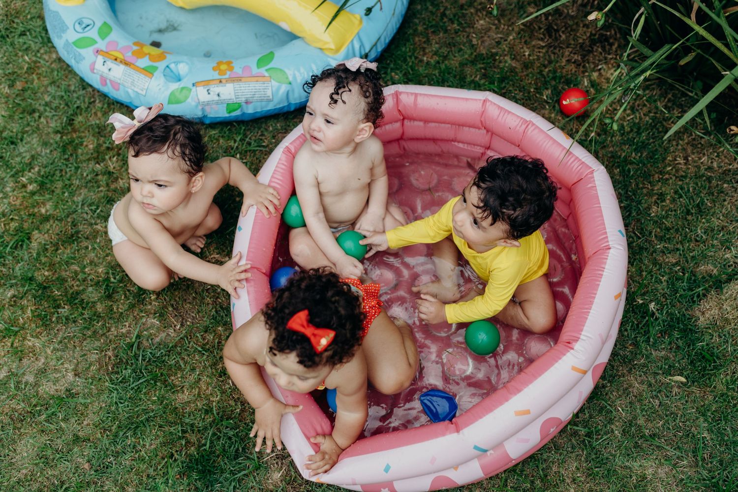 Children enjoying playtime in an inflatable kiddie pool on green grass.