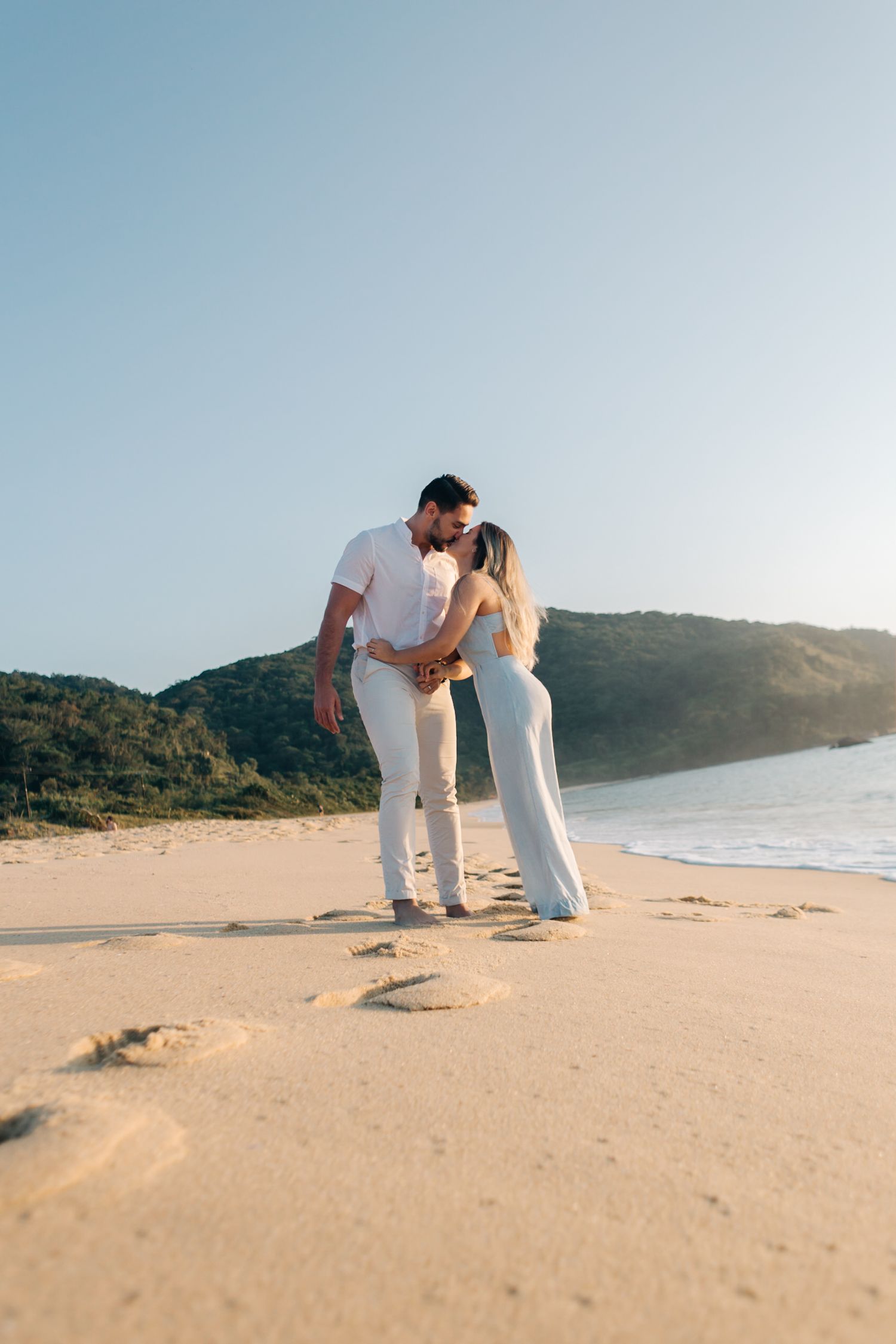 Romantic moment between couple in matching white outfits on a secluded beach.