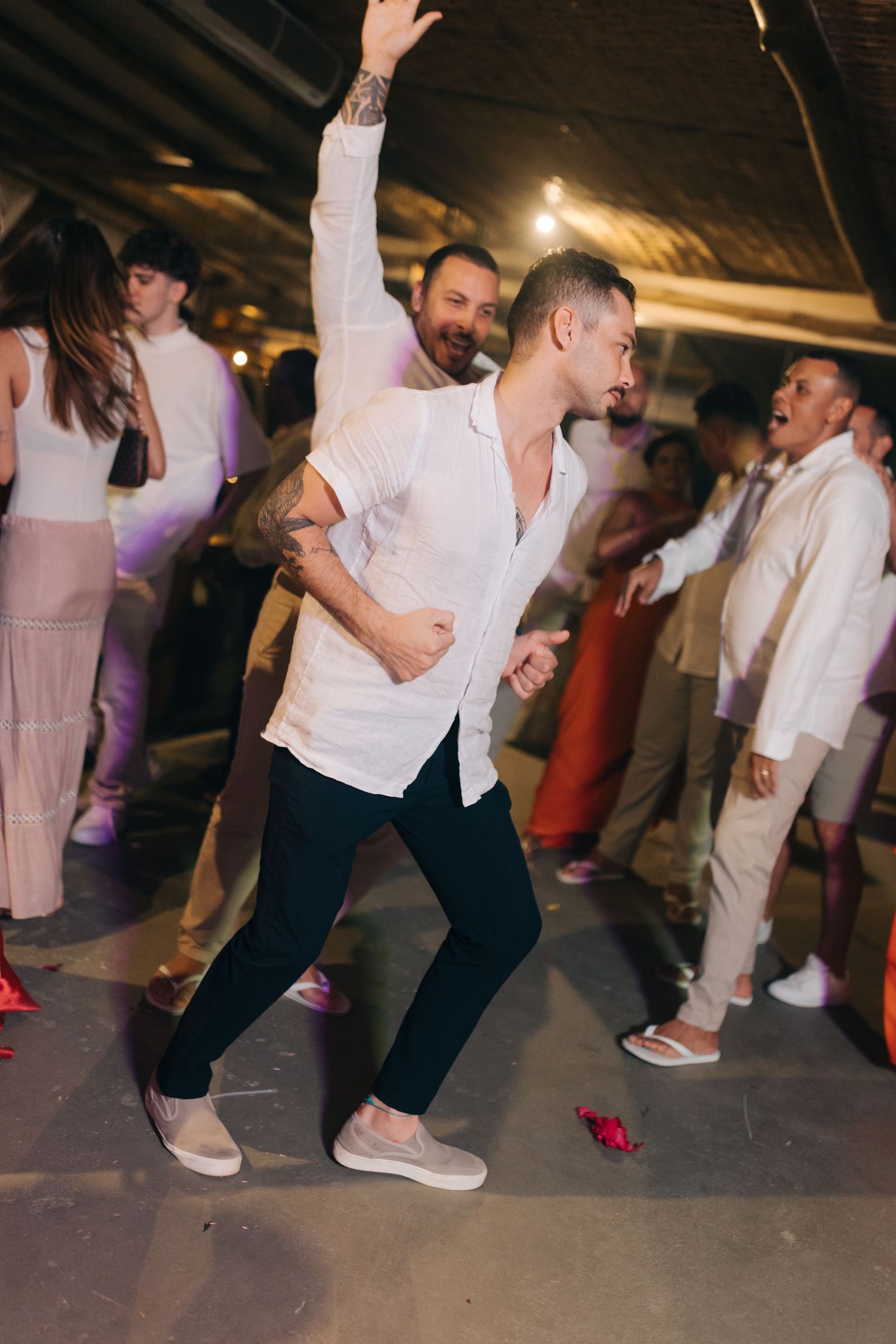 Wedding guest dances energetically in white shirt and dark pants during indoor reception.
