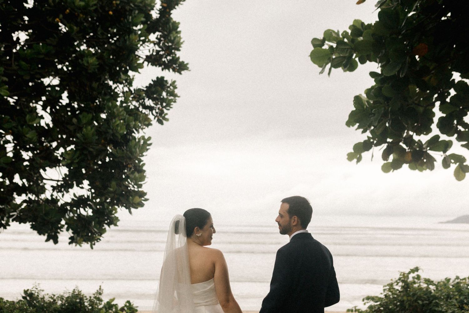Newlyweds share a private moment overlooking the ocean during sunset.