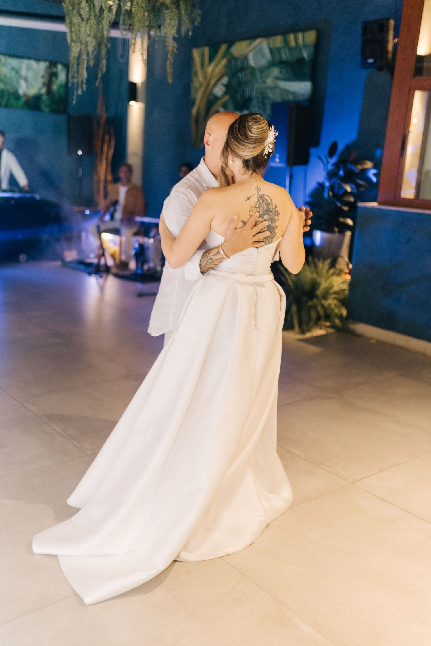 Bride in flowing white gown dancing alone on reception floor with romantic lighting.