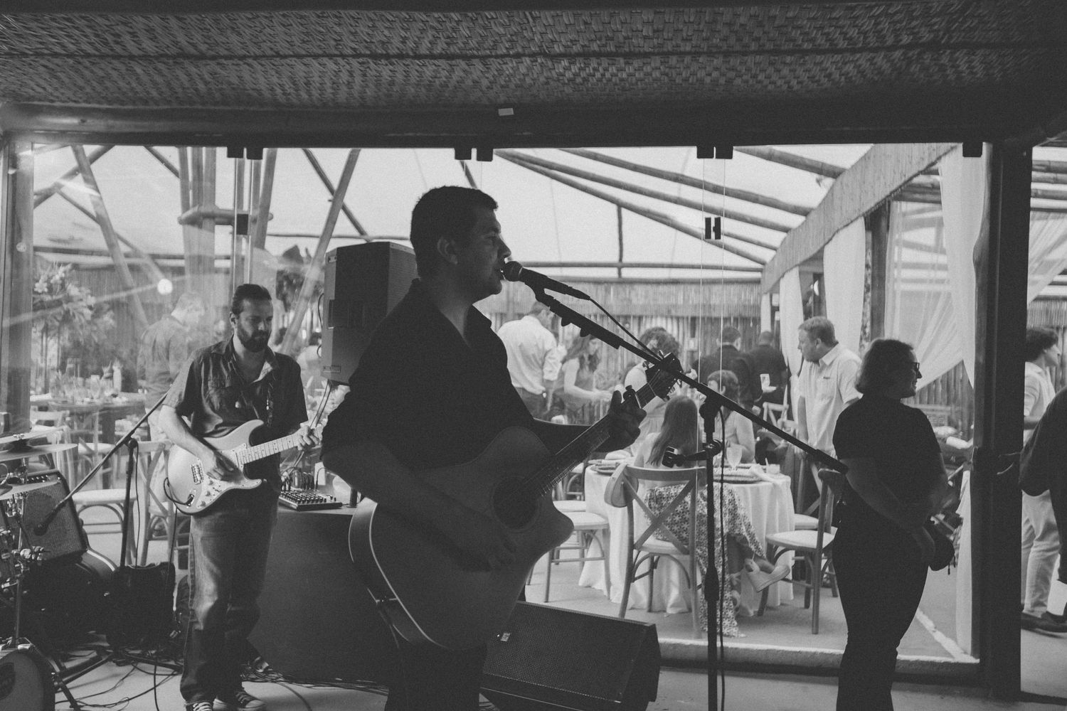 Silhouettes of a band performing live music in front of large windows.