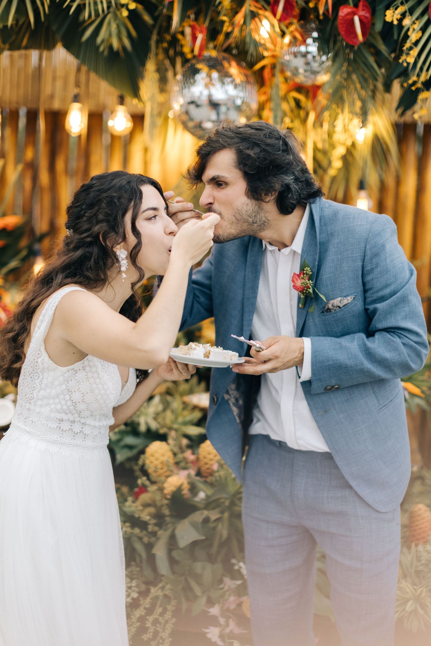 Couple shares a fun cake-feeding moment at their tropical themed wedding reception.