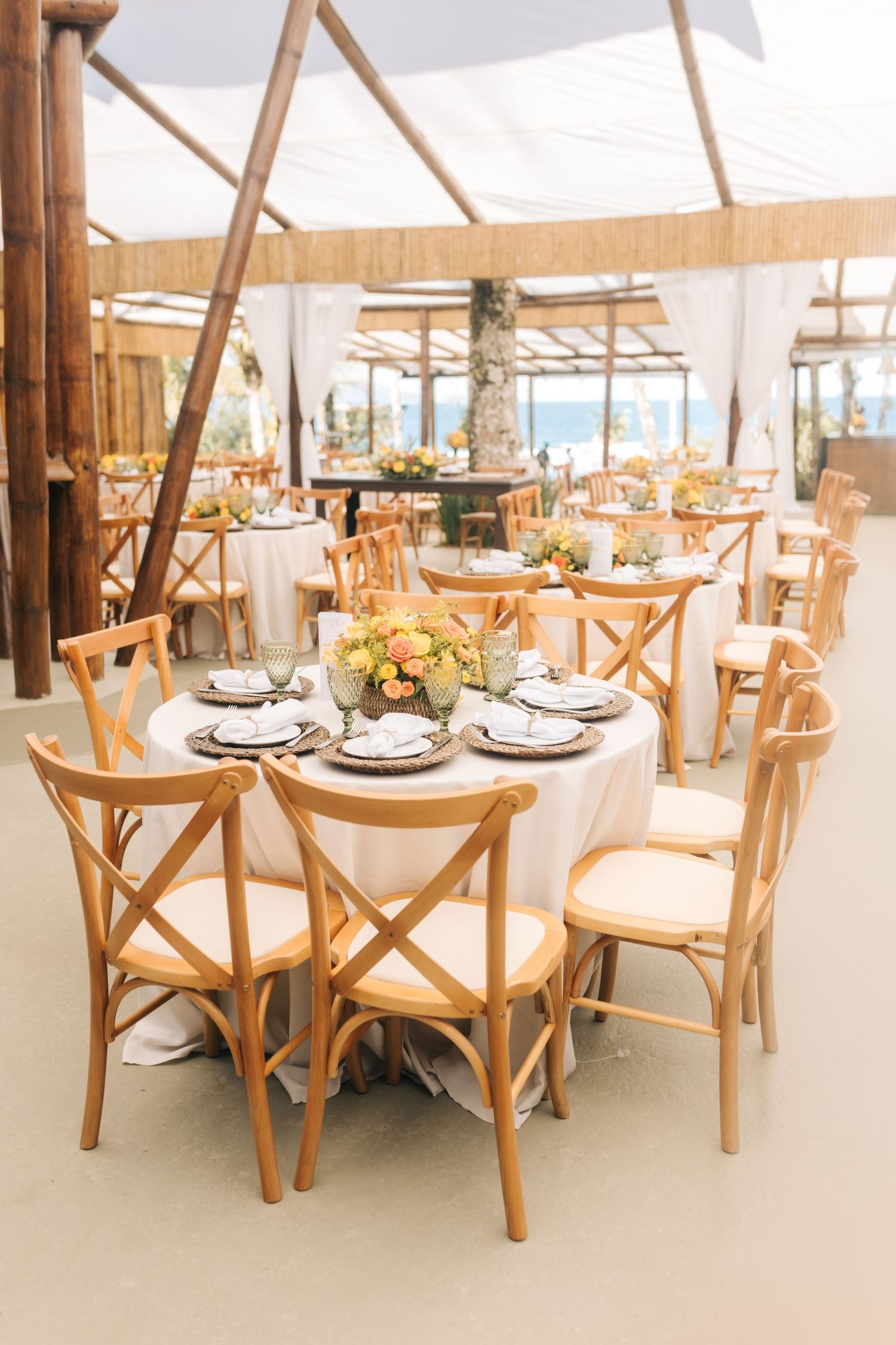Light-filled reception venue with wooden cross-back chairs and round tables set for dining.