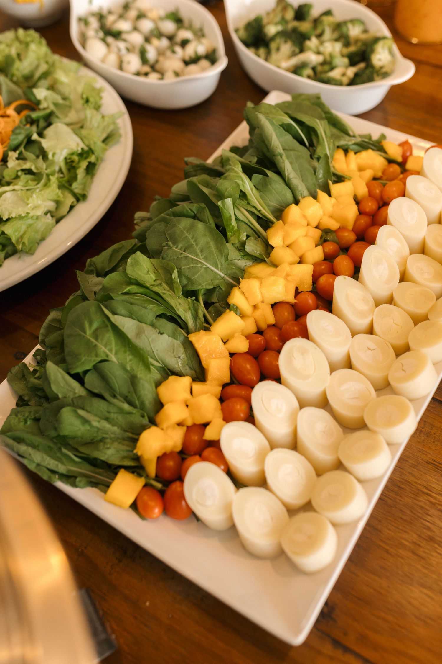 Fresh appetizer platter with greens, cheese, mango and cherry tomatoes arranged on white plate.
