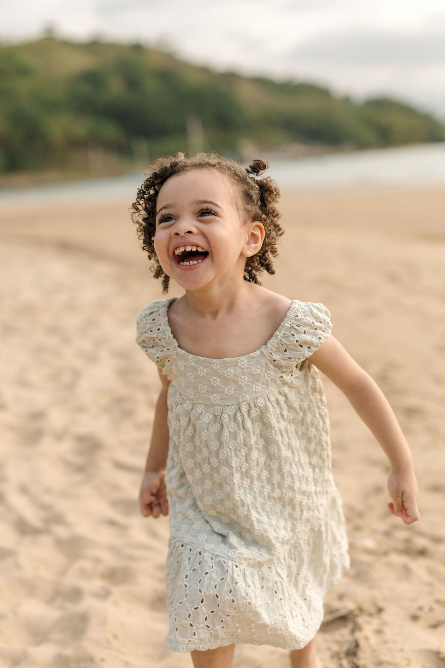 A happy child wearing a delicate white dress runs and laughs while playing on a sandy beach.