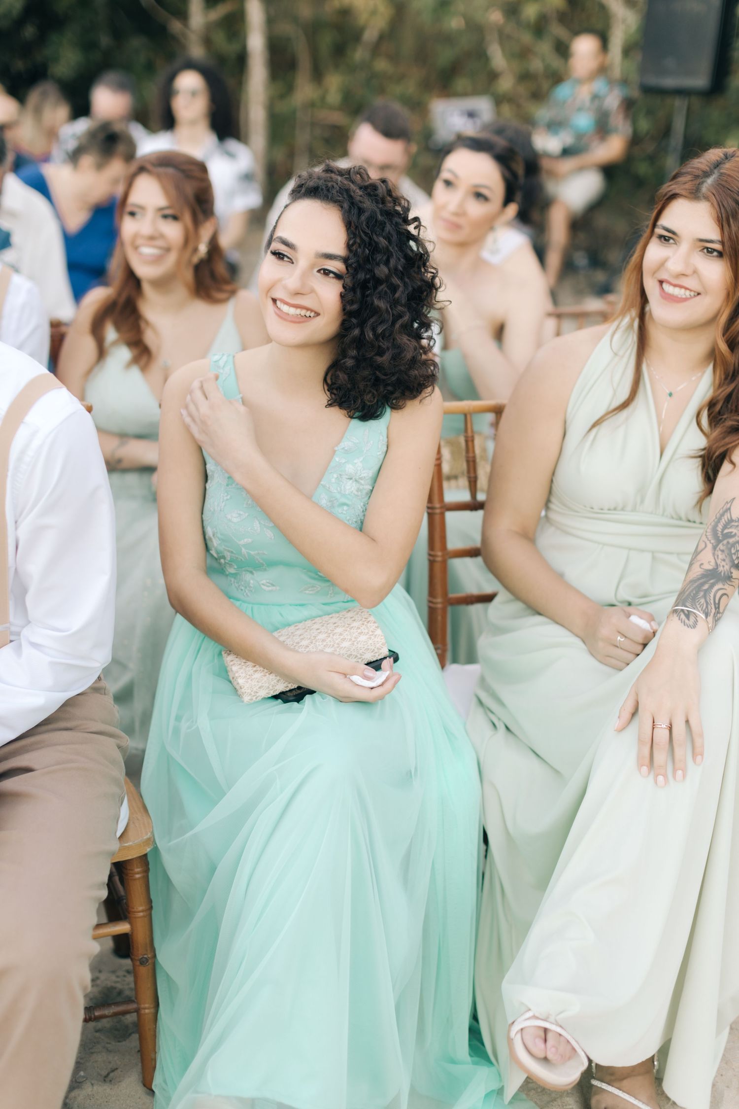 Bridesmaids in pastel mint and sage dresses smile during an outdoor wedding celebration.
