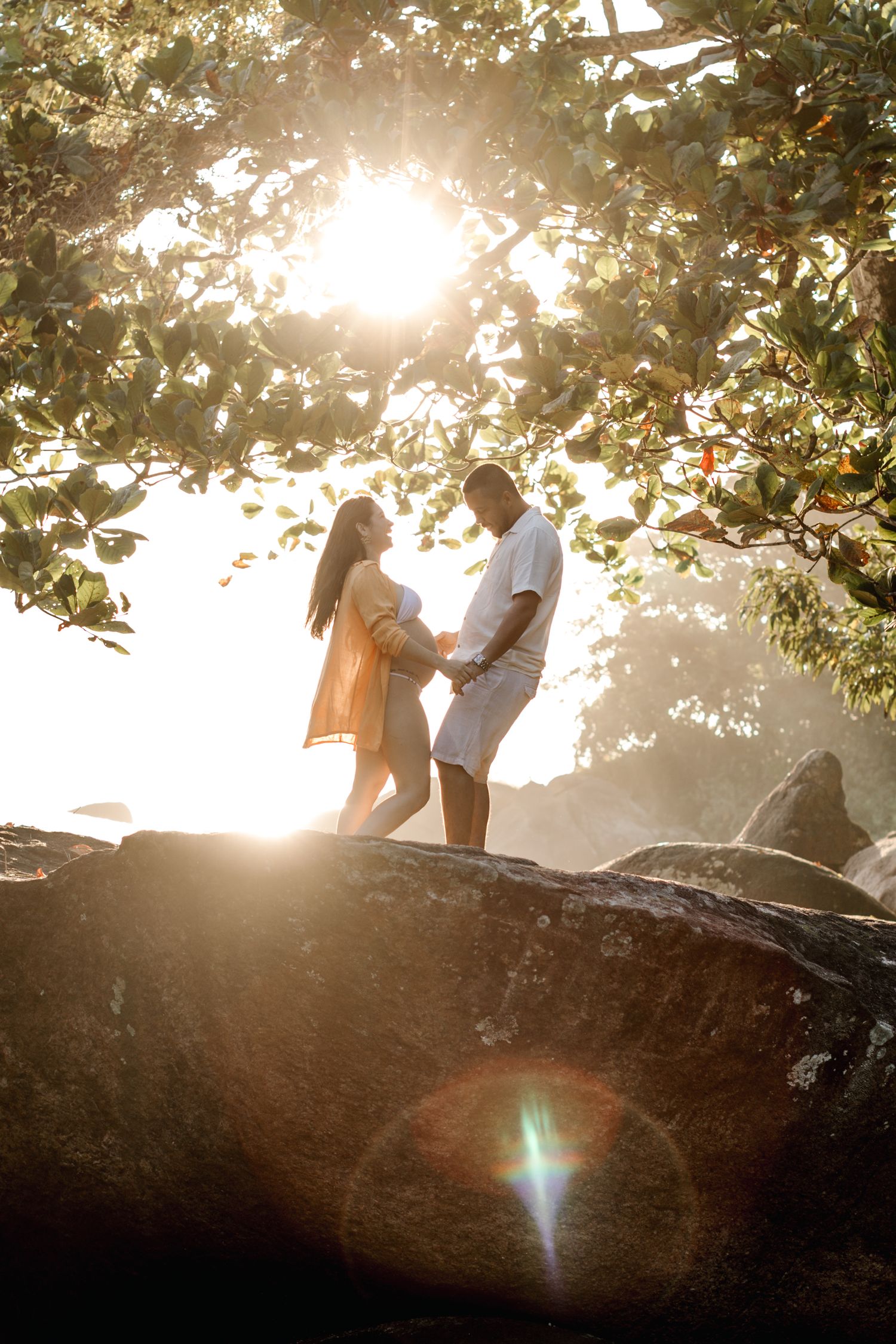Backlit couple stands on large rock formation during golden hour.