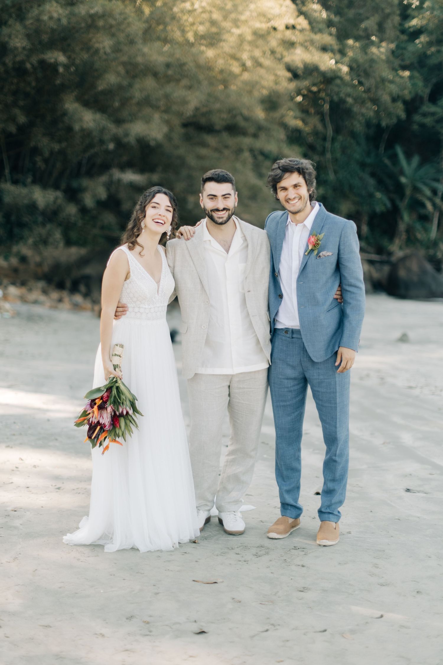 Small wedding group in white and blue attire laughs together on beach during photo session.