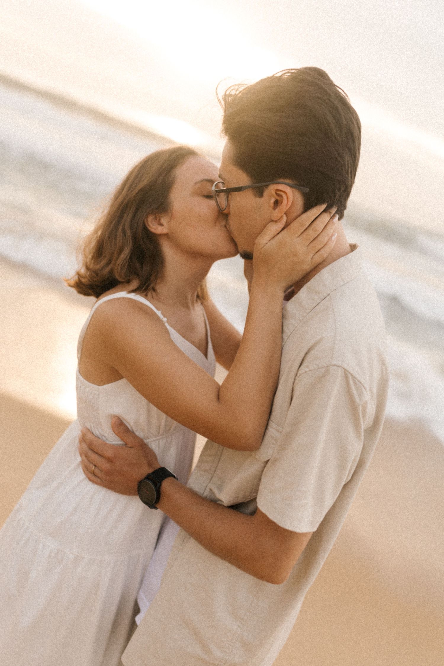 A tender moment between a couple sharing a passionate kiss on the beach at sunset.