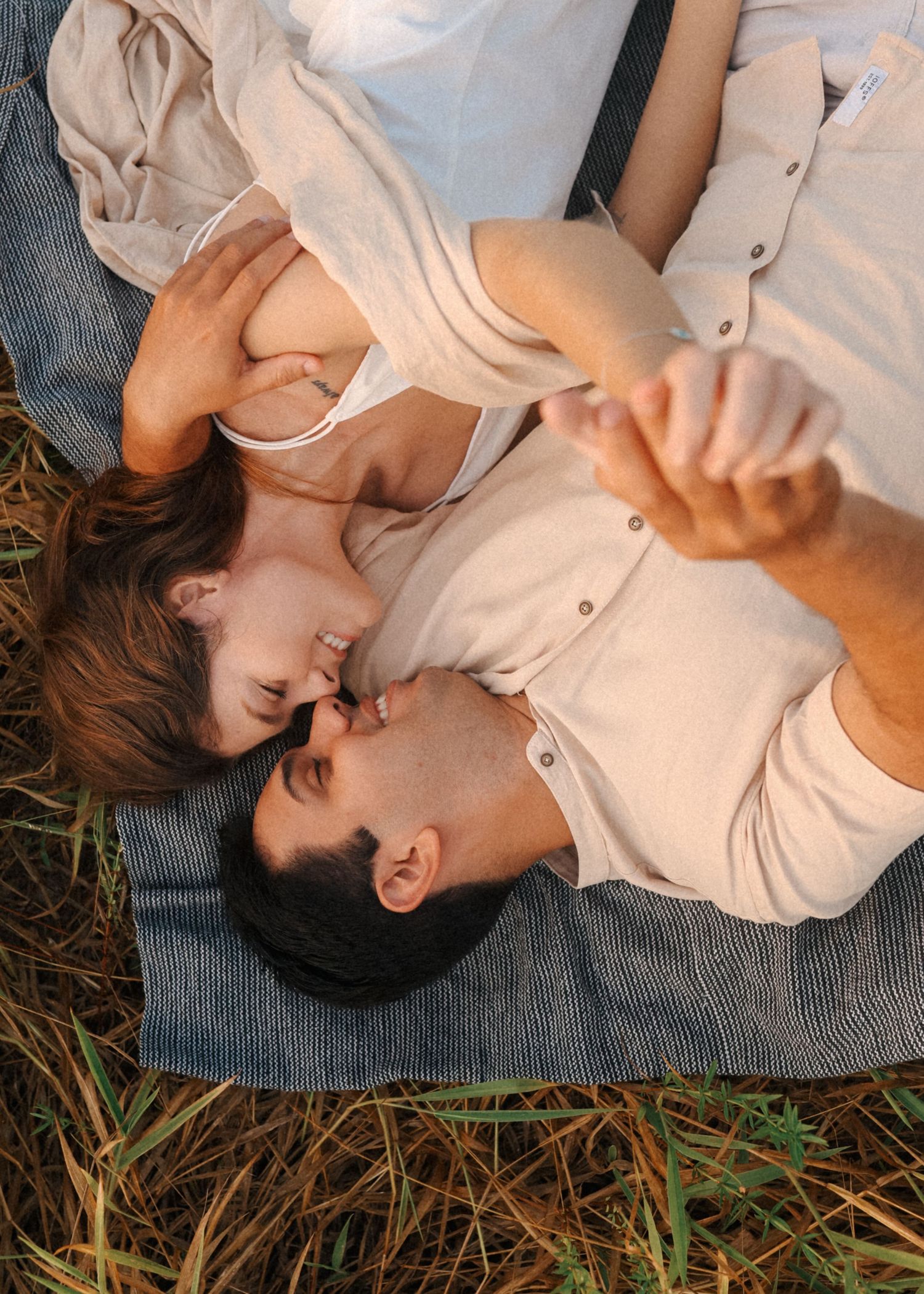 Intimate couple's portrait session on a blue blanket amidst wild grass.