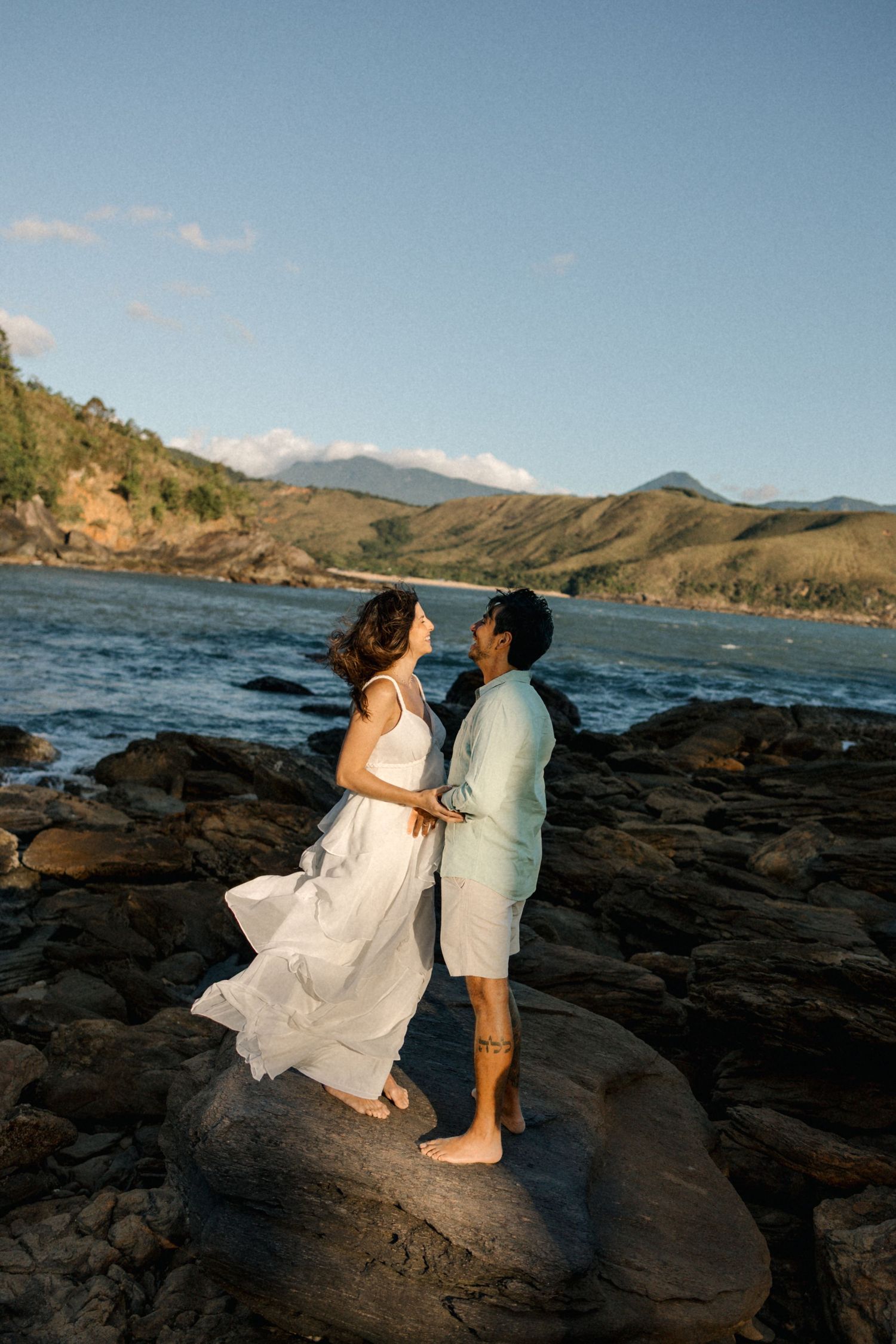 Two people share an intimate moment on black volcanic rocks by the ocean.