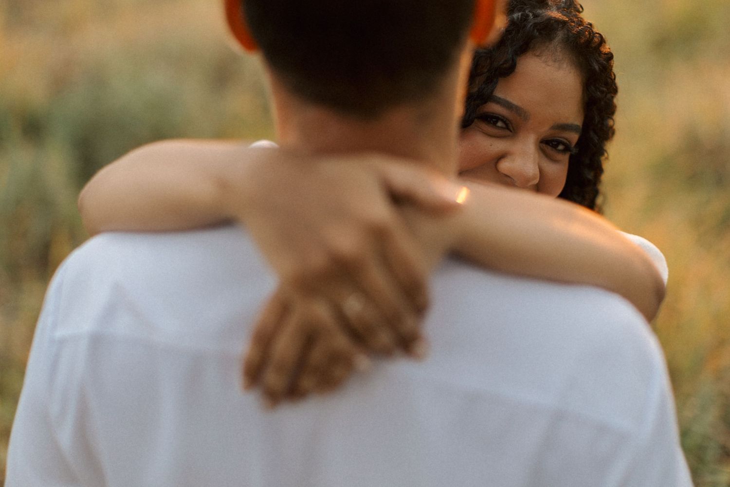 A loving embrace between two people backlit by warm sunlight in an outdoor setting.