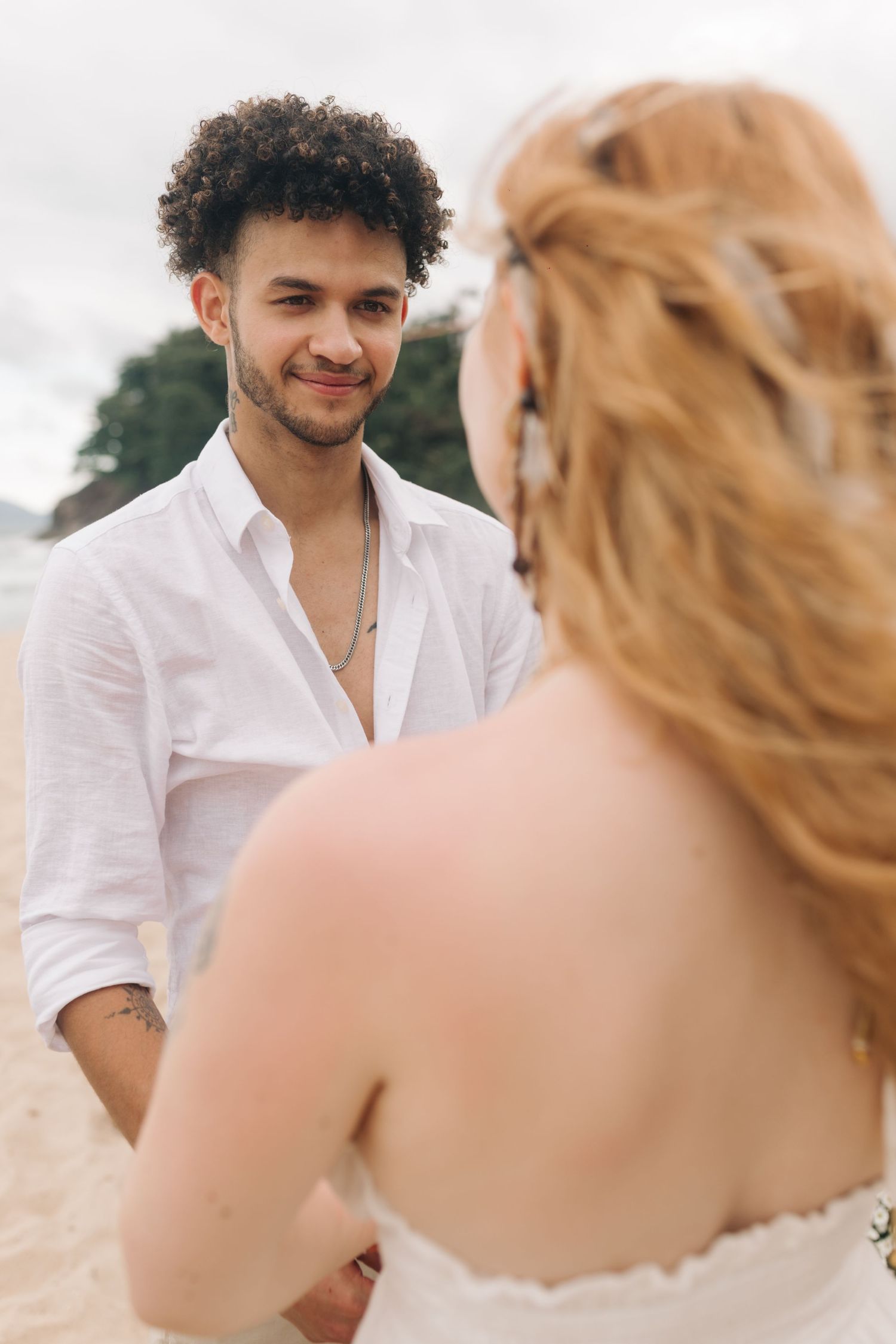 A romantic beach scene with two people in white clothing sharing a tender moment against an ocean backdrop.