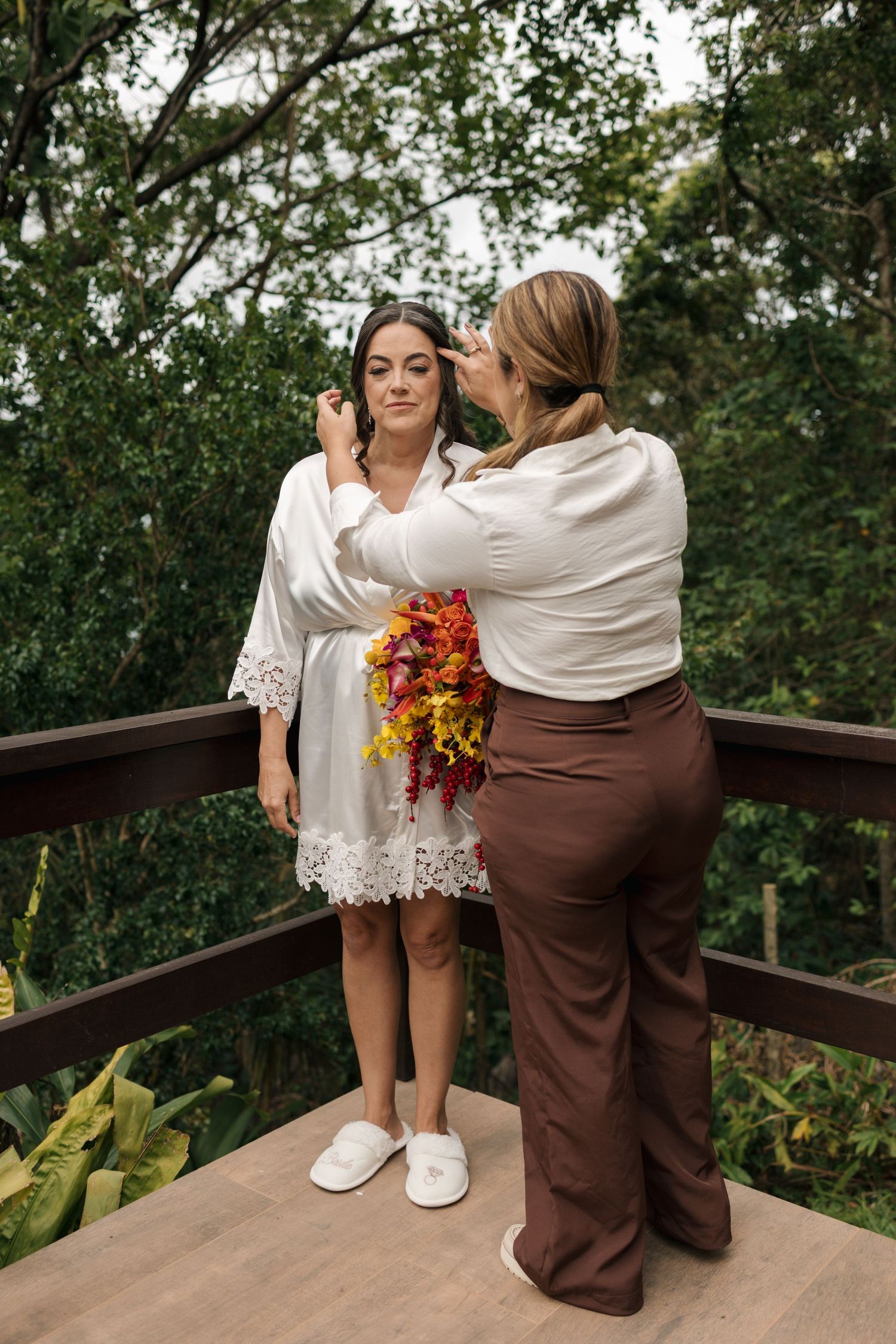 Two people share an intimate moment on a wooden deck surrounded by greenery.