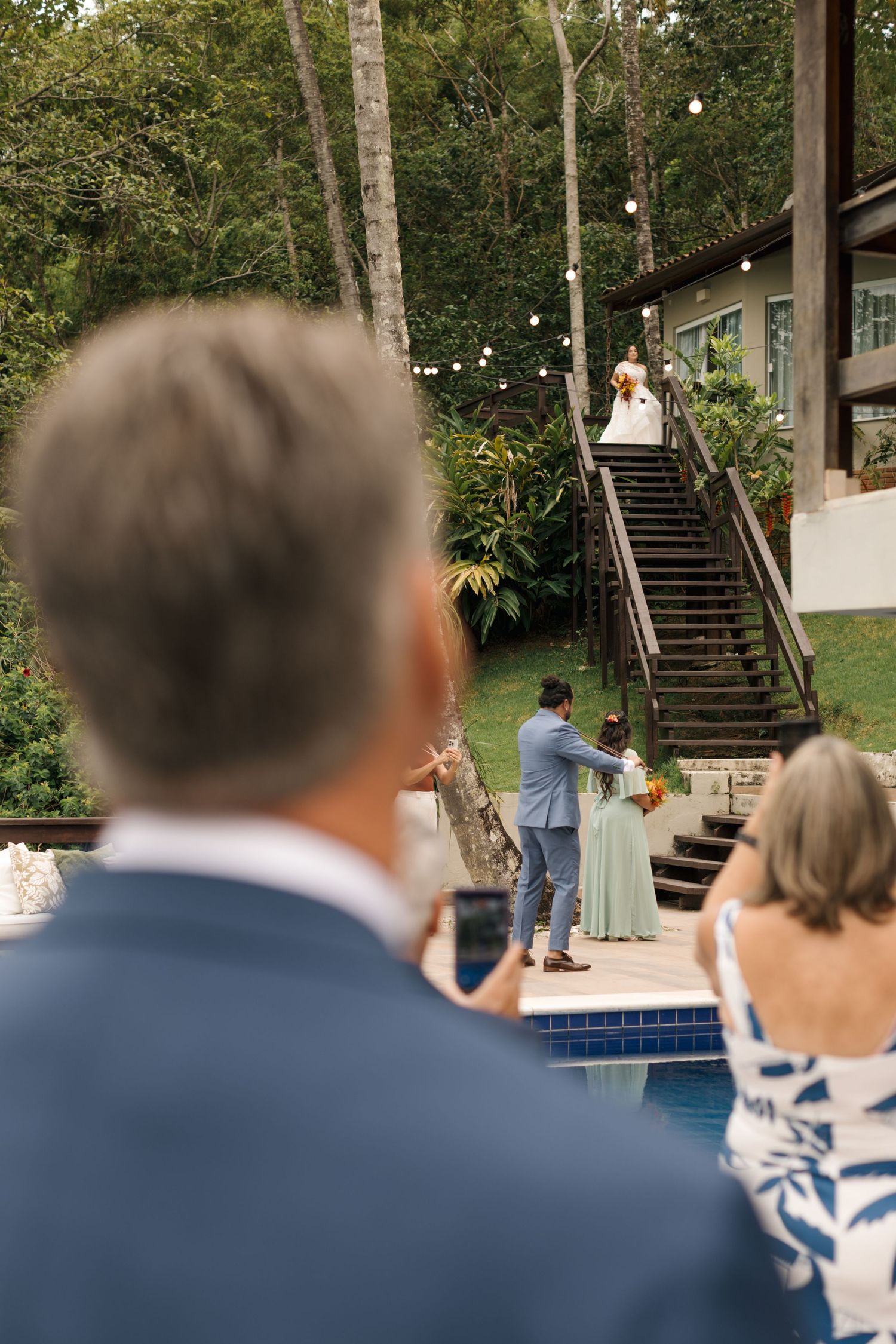 Outdoor wedding venue with wooden stairs and string lights among trees.
