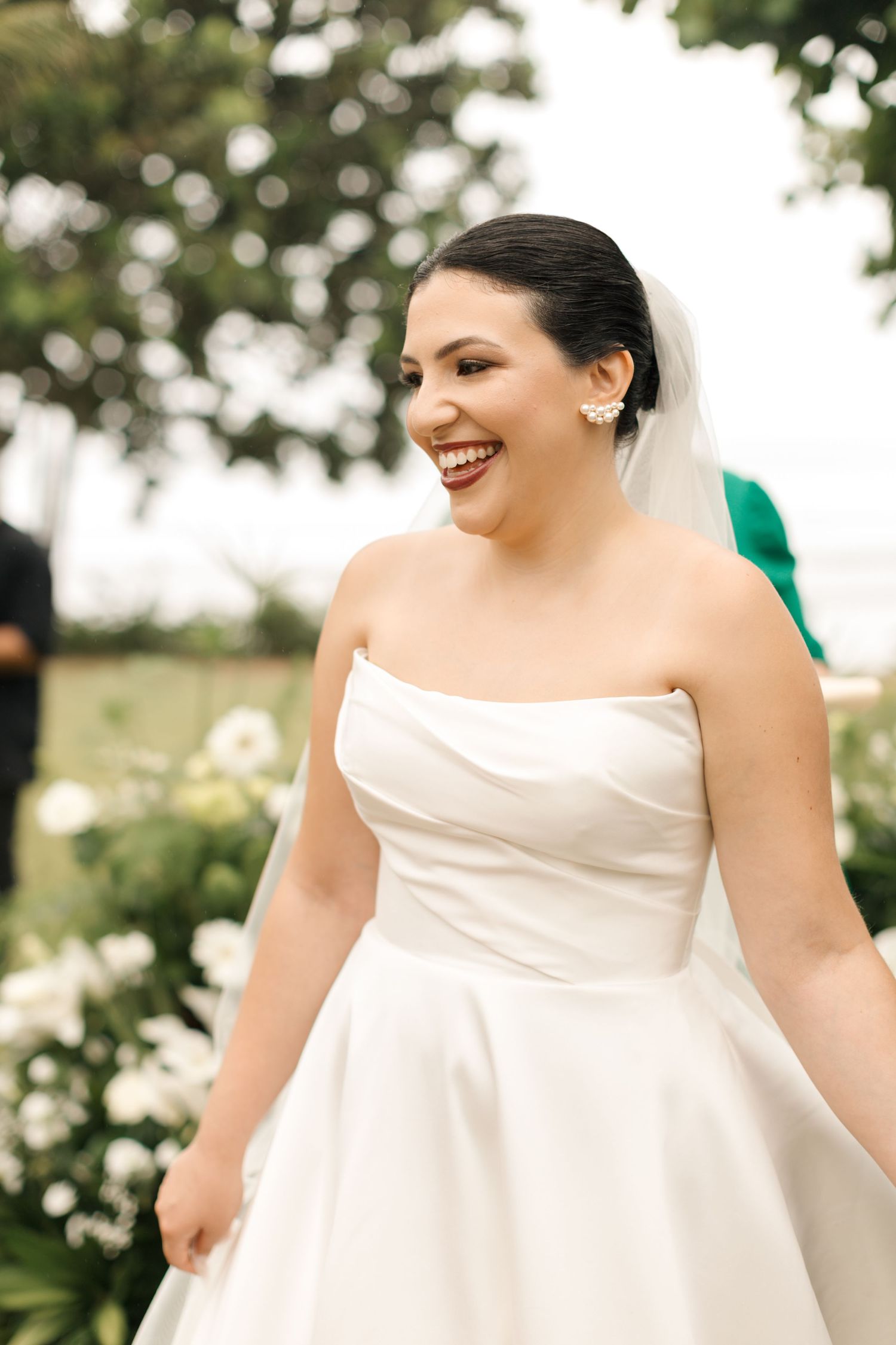 A radiant bride in a classic white strapless gown laughs joyfully during her wedding day.
