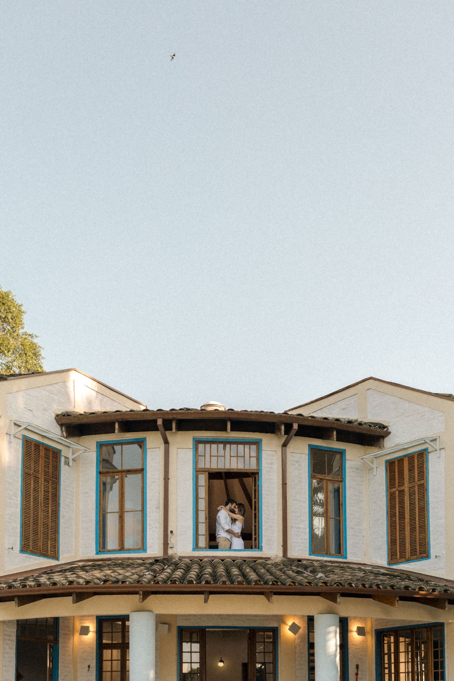White Mediterranean mansion features a curved balcony and wooden shutters with pool view.