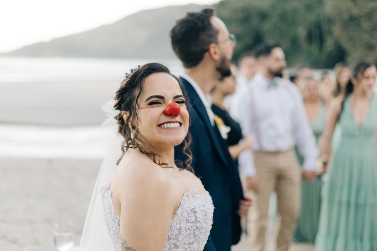 Beach wedding celebration with guests wearing colorful attire and red noses.