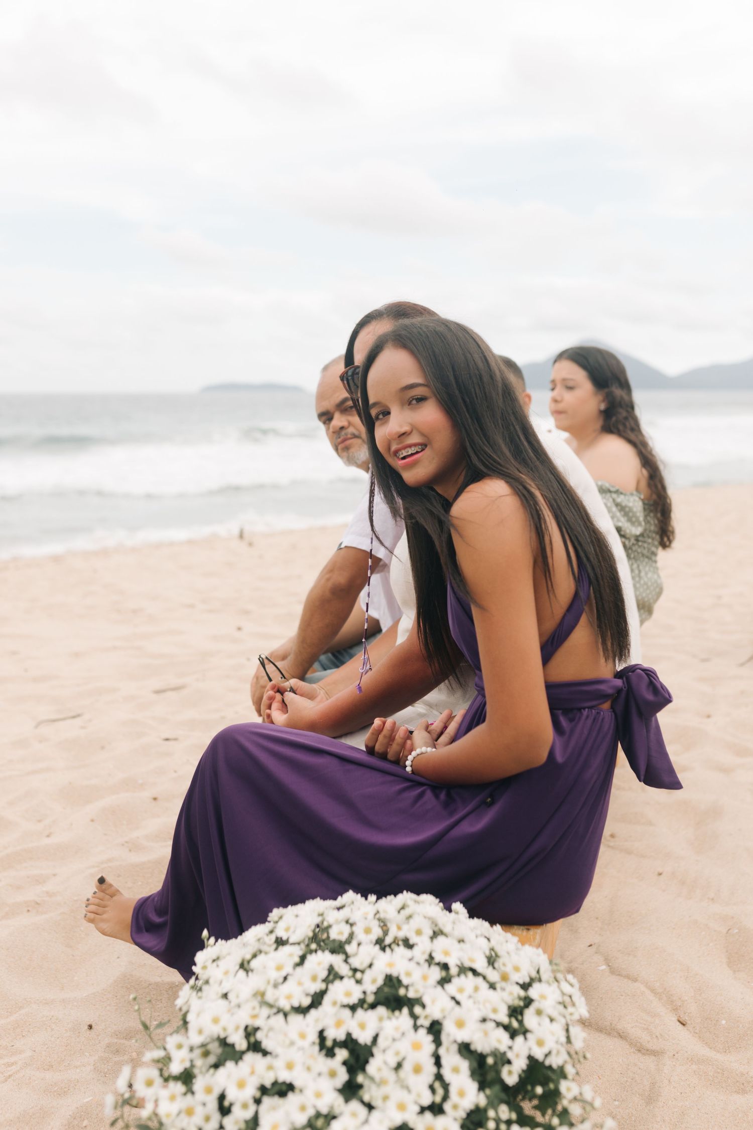 Wedding guests in purple dresses seated near white floral arrangements on beach.