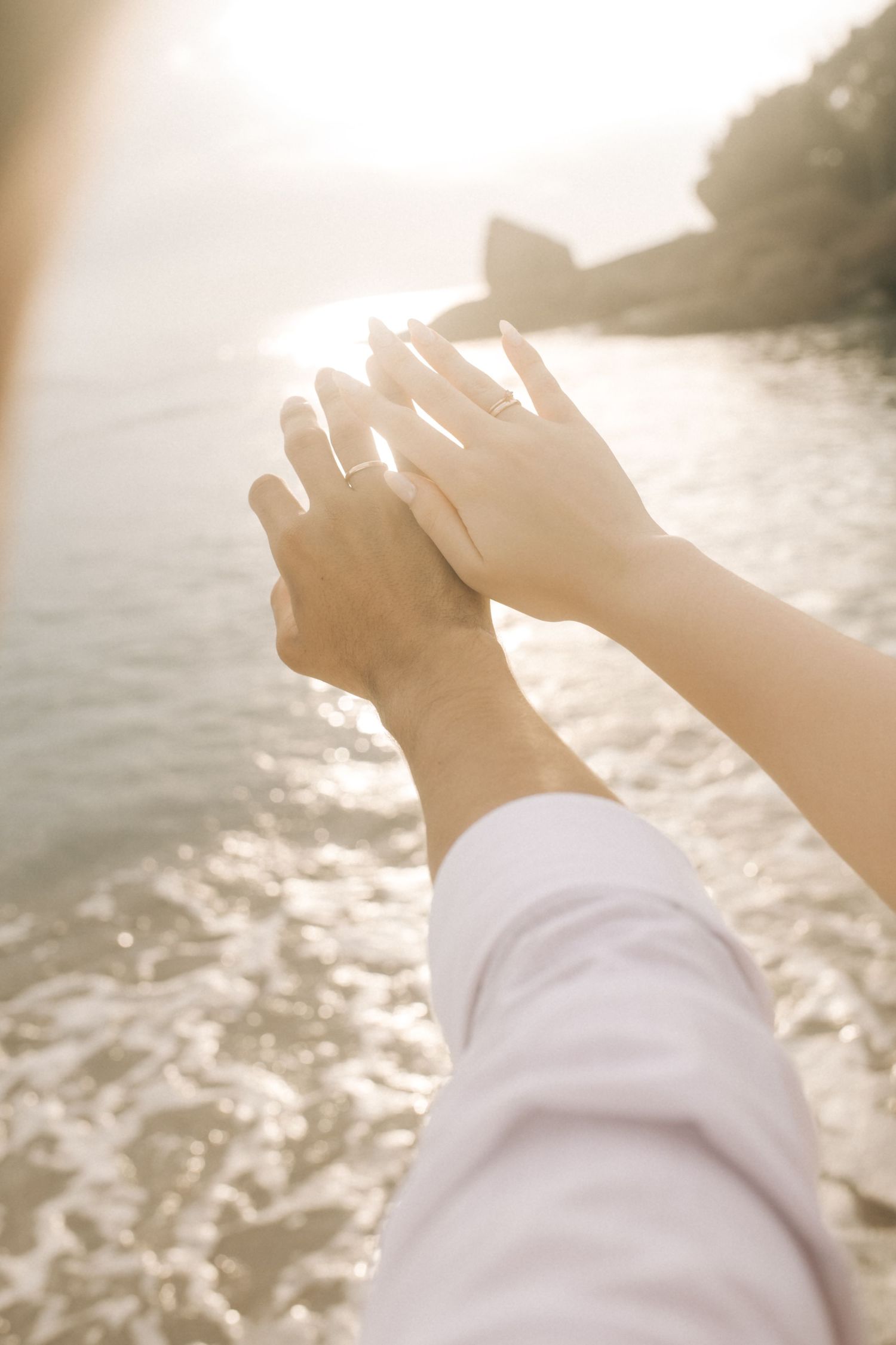 Two hands reach toward each other against a sunset ocean background.