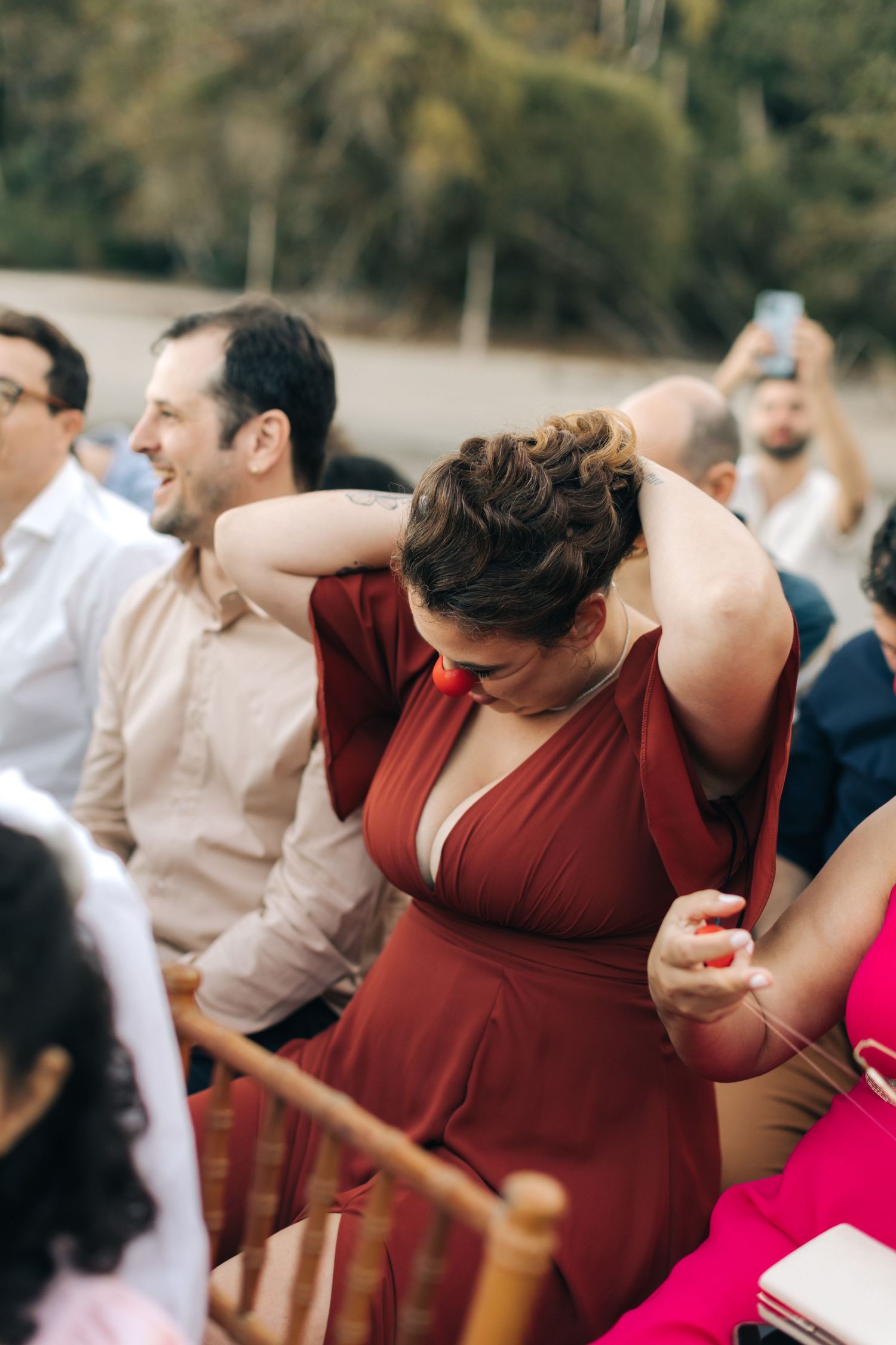 Wedding guests in burgundy dresses sharing laughs during outdoor celebration.